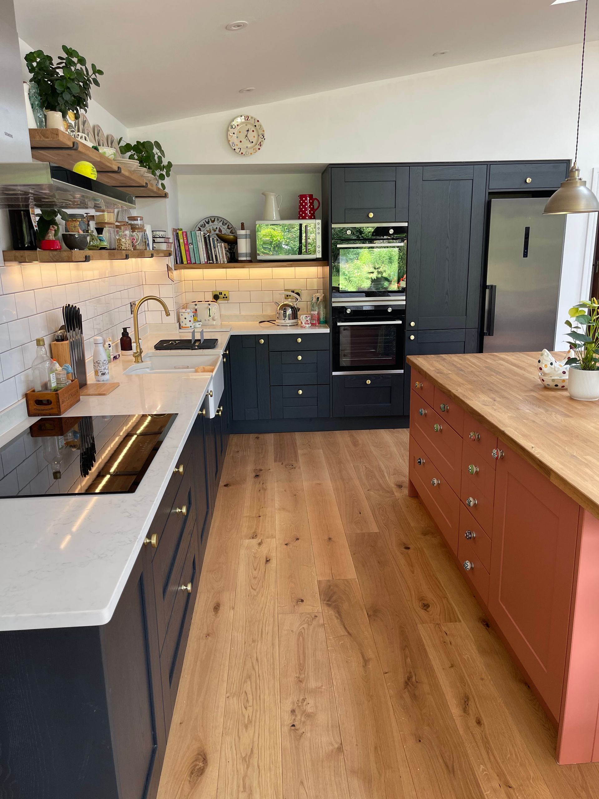 A modern kitchen with dark blue cabinets, a terracotta-colored island, light wood floors, and open shelving.