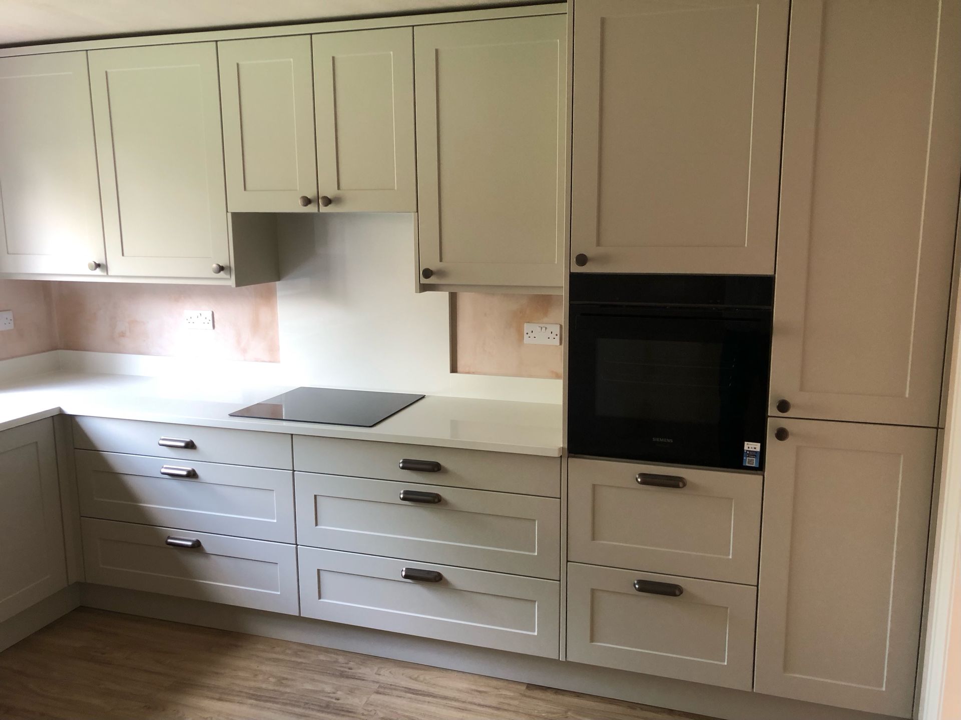 Modern kitchen featuring light grey shaker-style cabinets, a black built-in oven, and a dark induction hob on white counters.
