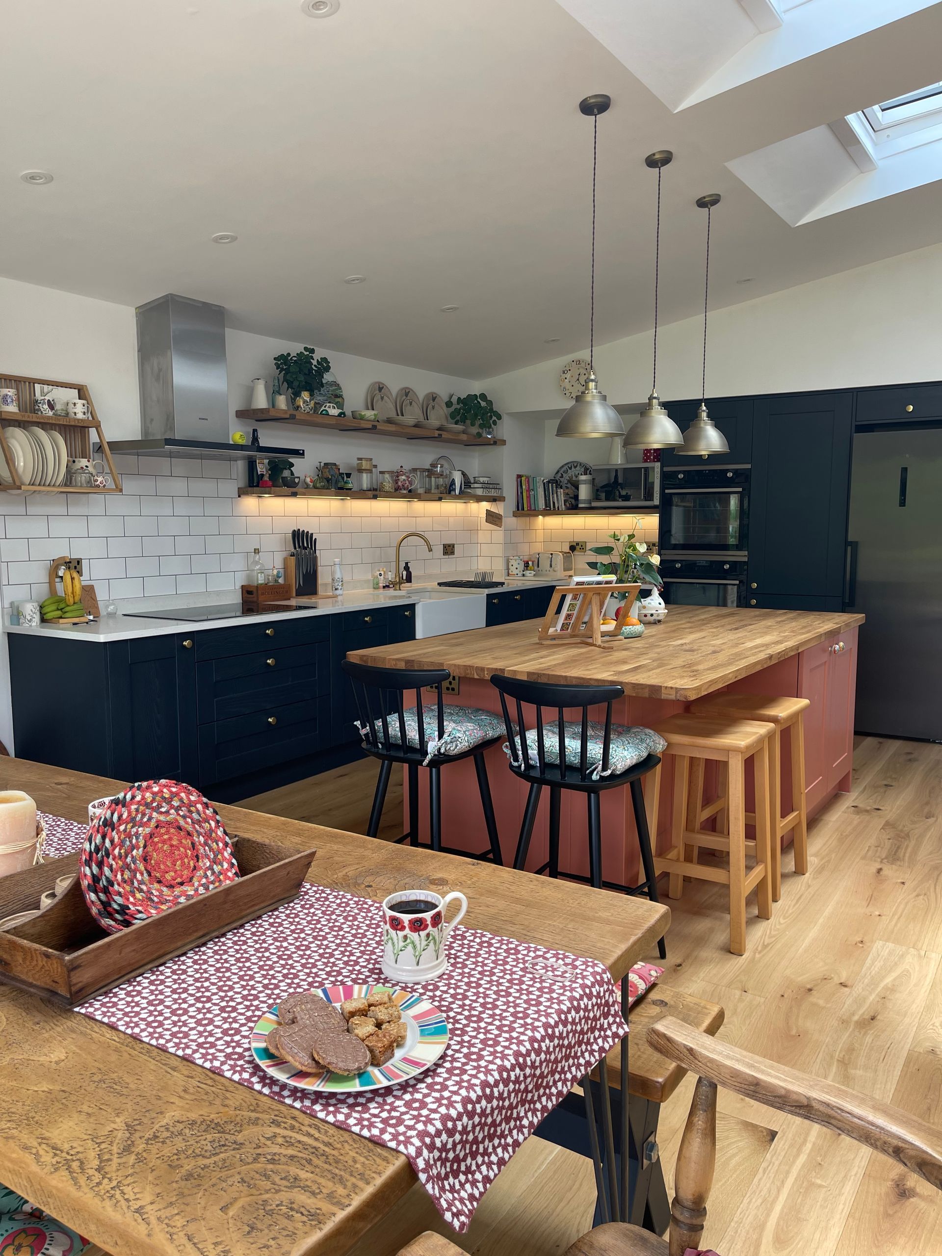 Modern kitchen with blue lower cabinets, a terracotta island, wooden countertops, and a dining table with a patterned cloth.