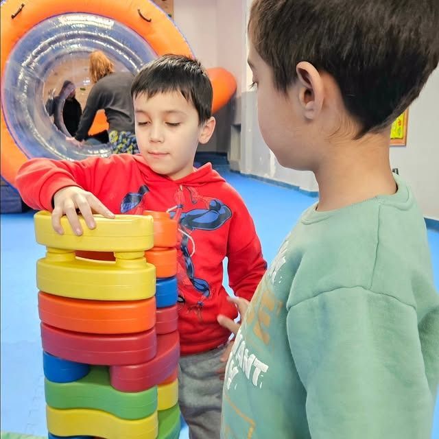 Dos niños pequeños juegan con bloques de colores apilados en el interior.