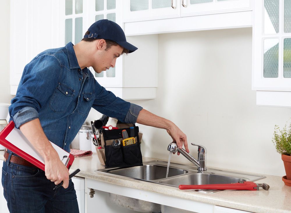 A Plumber Is Fixing A Faucet In A Kitchen — Tim Larkin Plumbing and Excavations in Laurieton, NSW