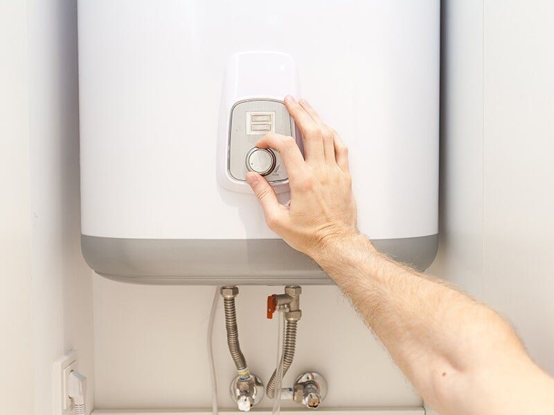 A Person Is Twisting Knob On A Water Heater — Tim Larkin Plumbing and Excavations in Wauchope, NSW