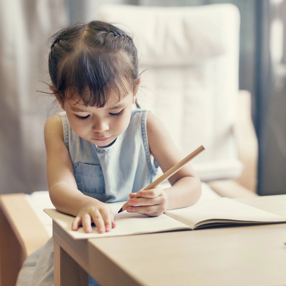 A little girl is writing in a notebook with a pencil
