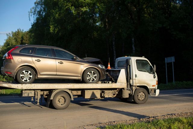 Grúa transportando un SUV color beige en una plataforma en la cuneta.