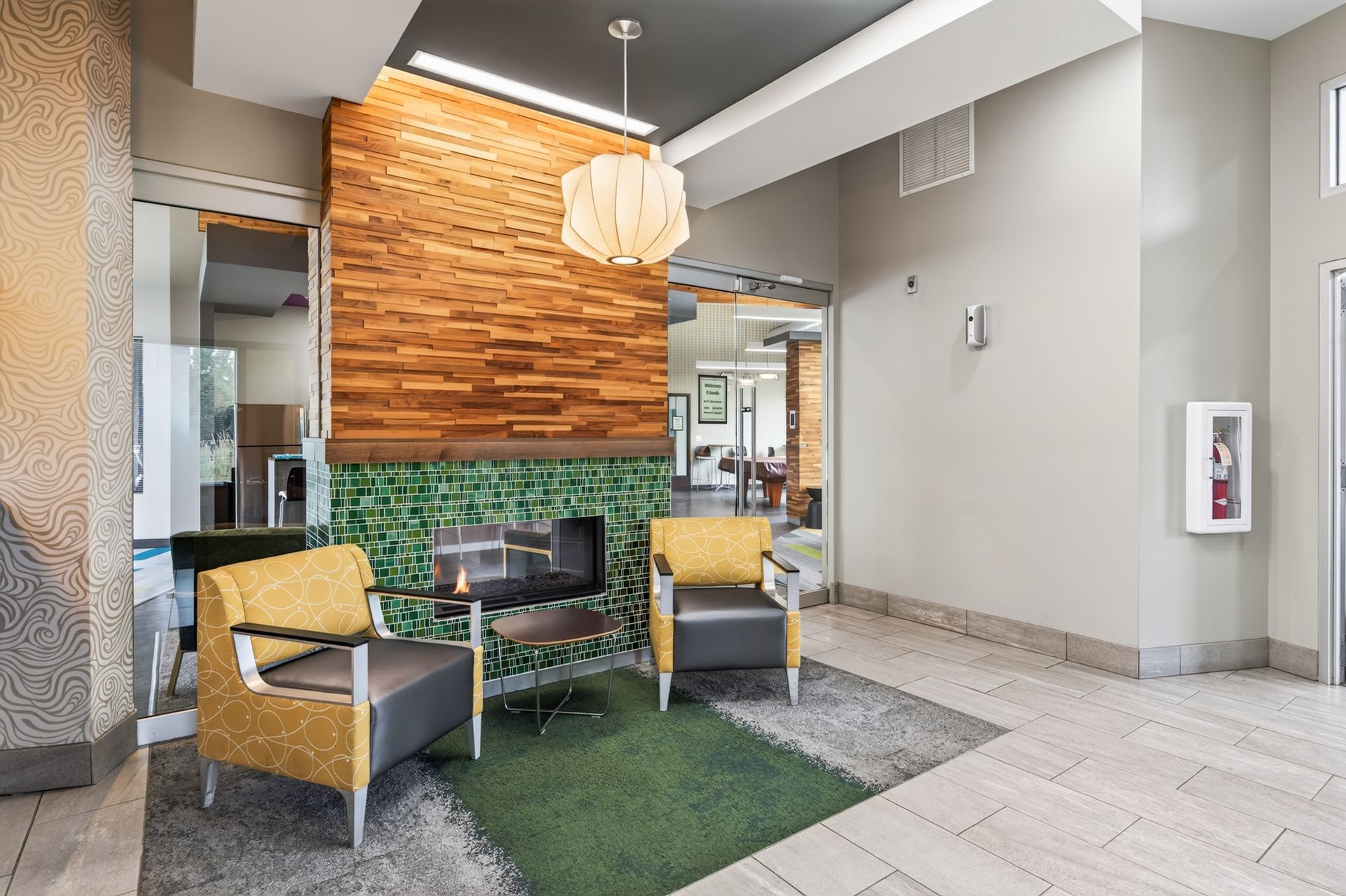 Modern lobby seating area with yellow chairs, green rug, wood accent wall, and hanging light