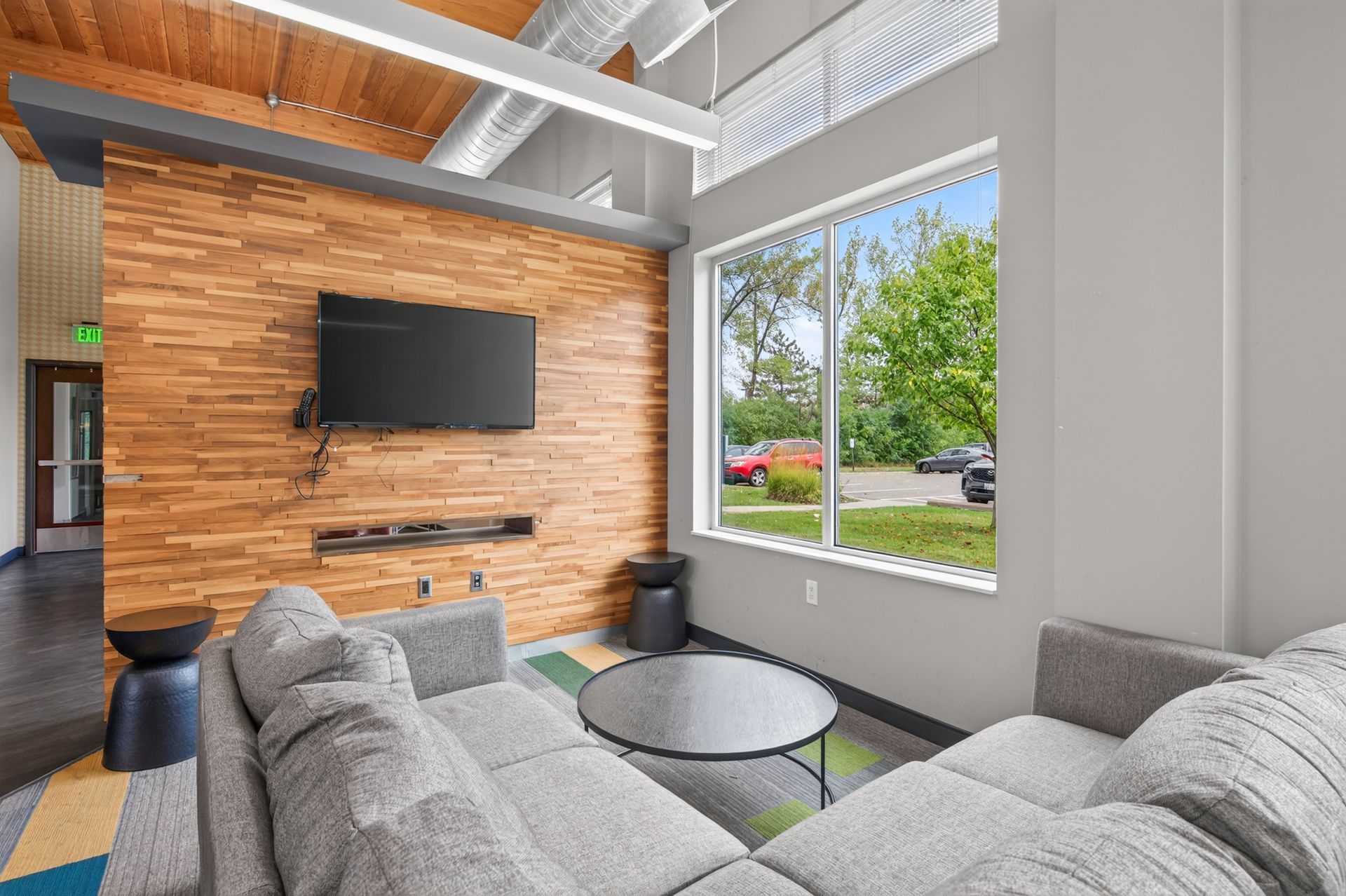 Modern living room with gray sectional, wall-mounted TV, wood accent wall, and large window view