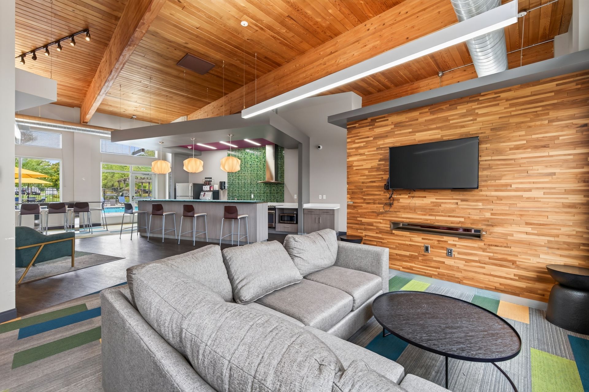 Modern open-concept living room with gray sectional, wood accent wall, wall-mounted TV, and vaulted wood ceiling