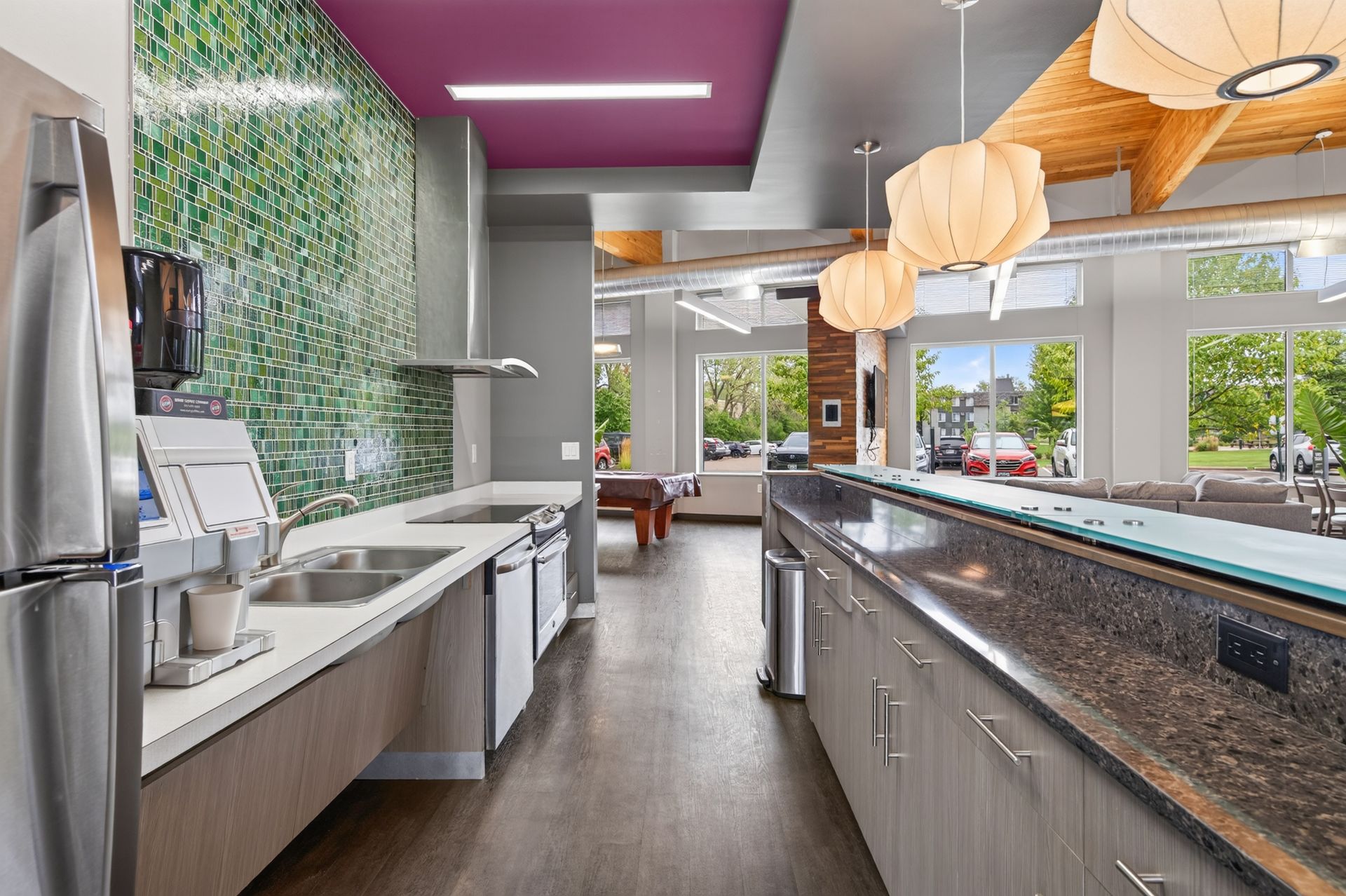 Modern kitchen with stainless appliances, large island, purple accent wall, and bright windows