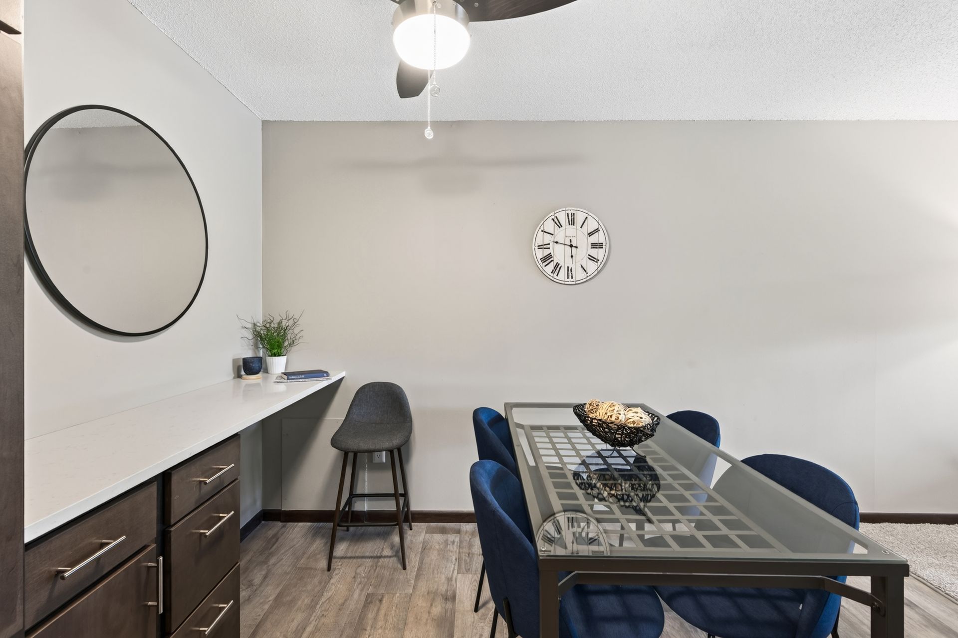 Modern dining room with gray table, blue chairs, wall clock, and round mirror