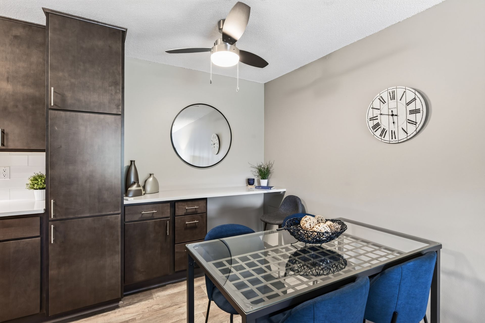 Modern dining room with dark cabinets, a glass-top table, blue chairs, and wall decor