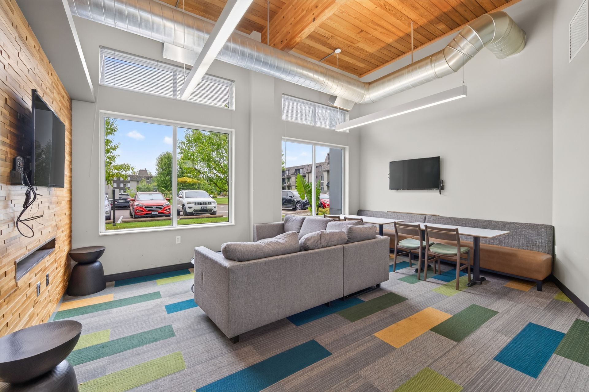 Modern living room with gray sofa, wall-mounted TV, large windows, and colorful rug