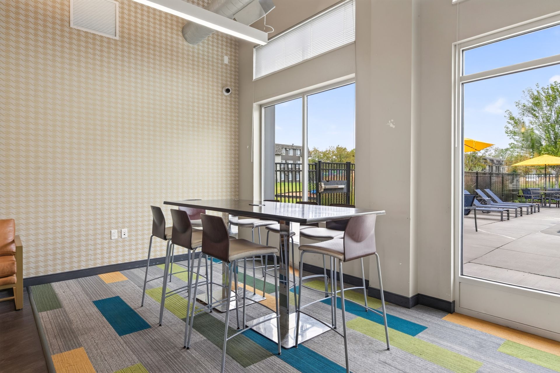 Bright café seating area with high tables, stools, and large windows overlooking an outdoor patio