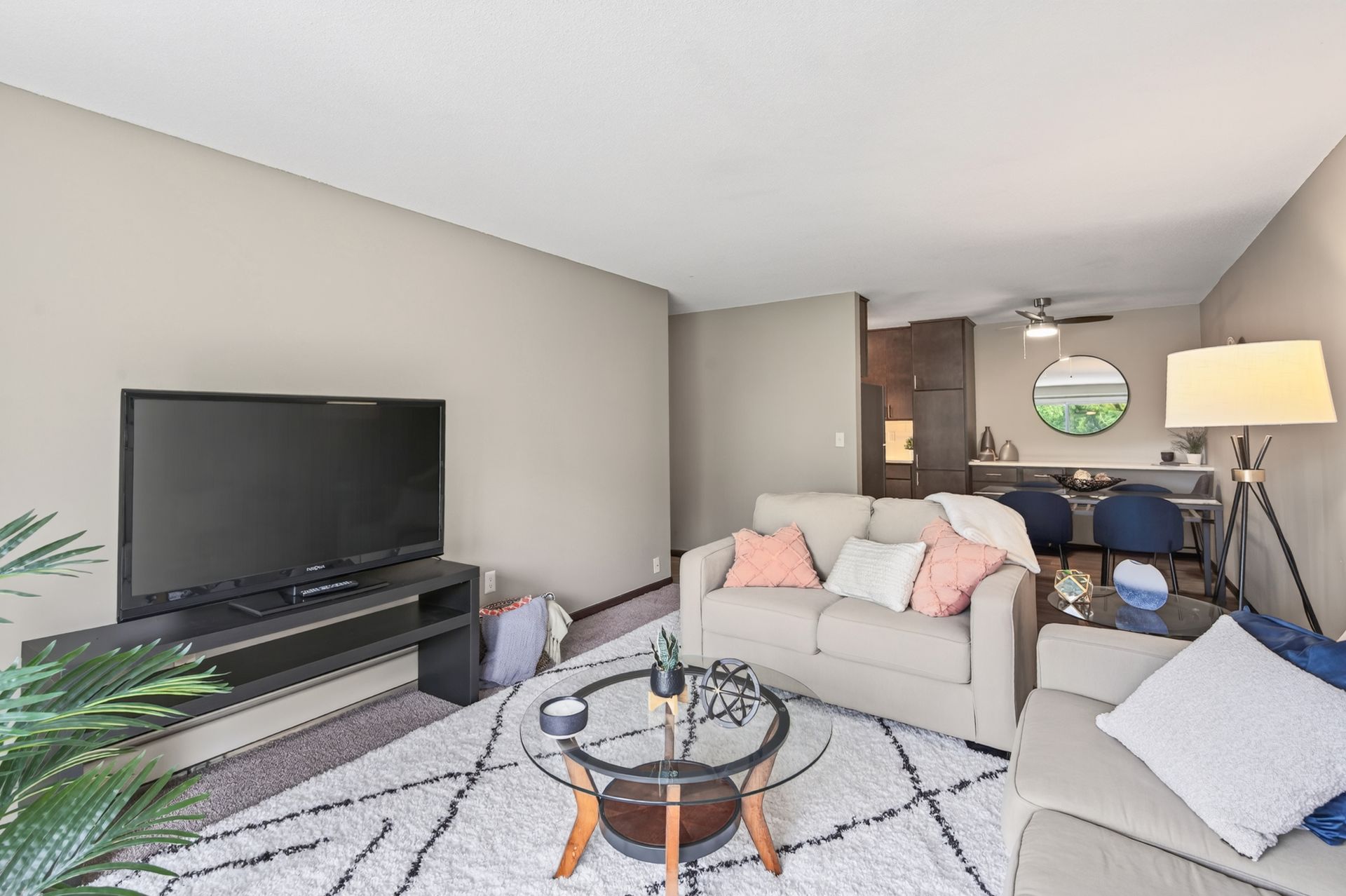 Bright living room with gray sofas, large TV, glass coffee table, and a dining area in back.