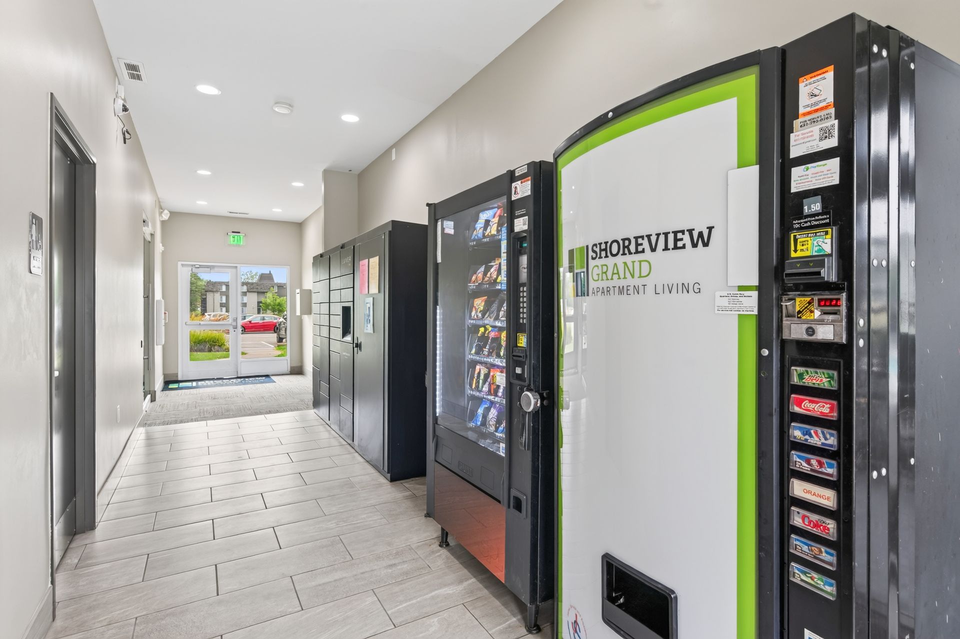 Hallway with row of vending machines, including a white and green machine, in a bright building corridor