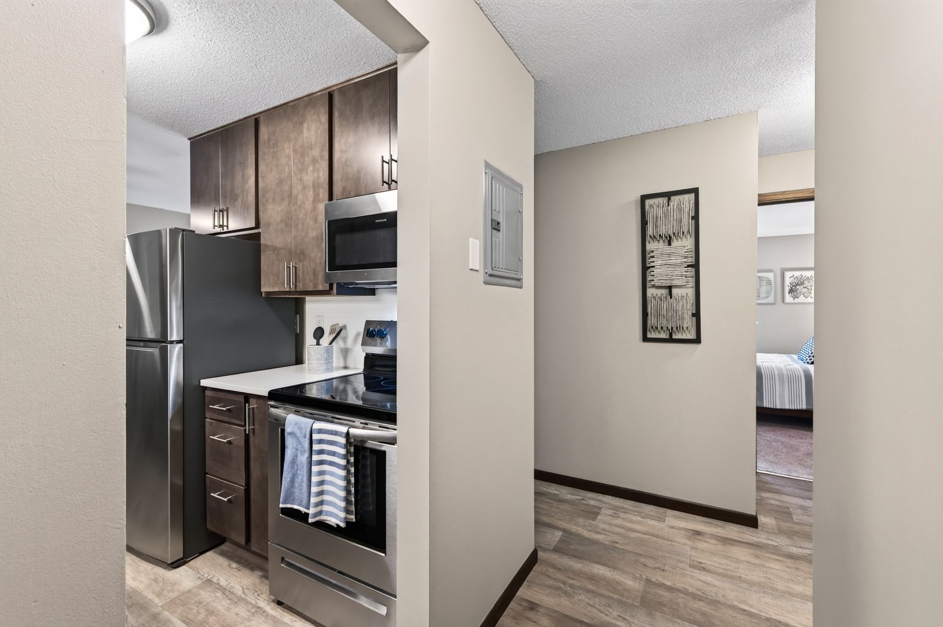 Small kitchen with stainless appliances and wood cabinets, opening to a hallway and bedroom.
