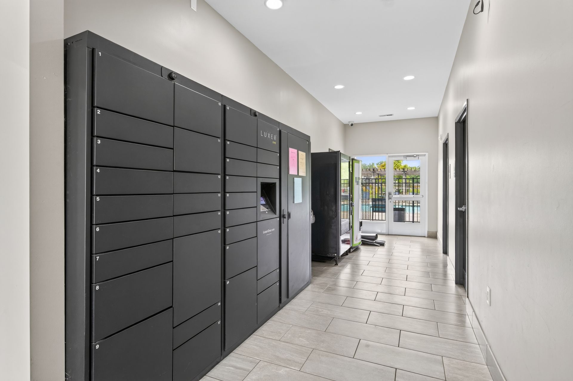 Modern apartment mailroom with black parcel lockers and a bright hallway leading to a glass door