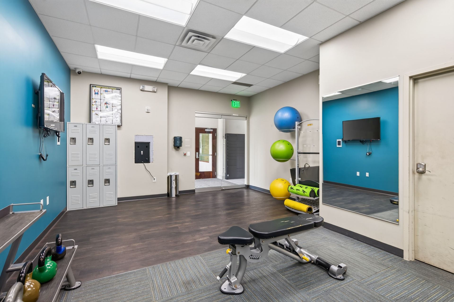 Fitness room with exercise bikes, stability balls, mats, lockers, and a wall-mounted TV