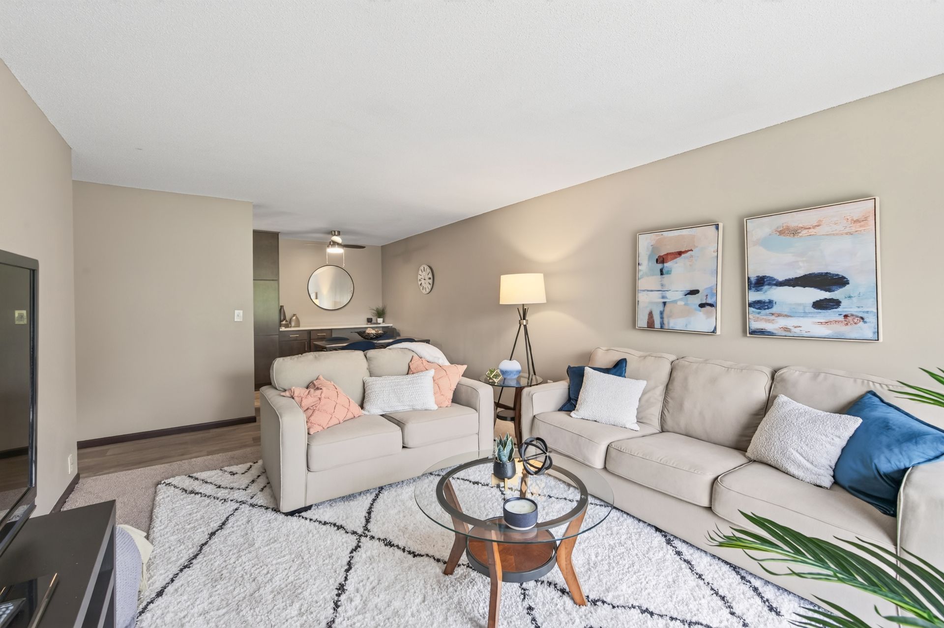 Bright living room with beige sofas, blue pillows, a lamp, artwork, and a round coffee table on a patterned rug