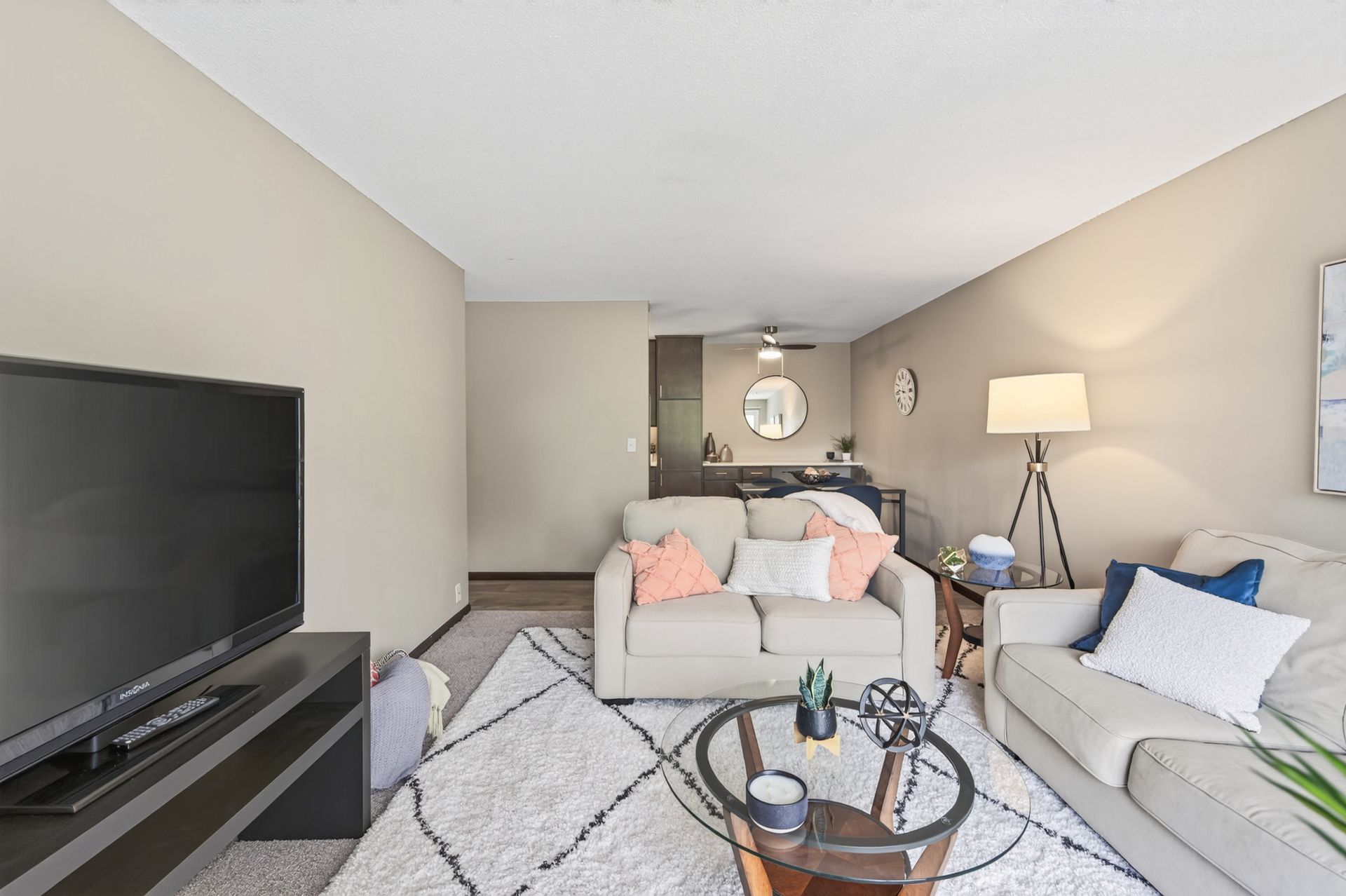 Bright living room with beige walls, gray sofas, TV, and a coffee table on a patterned rug.