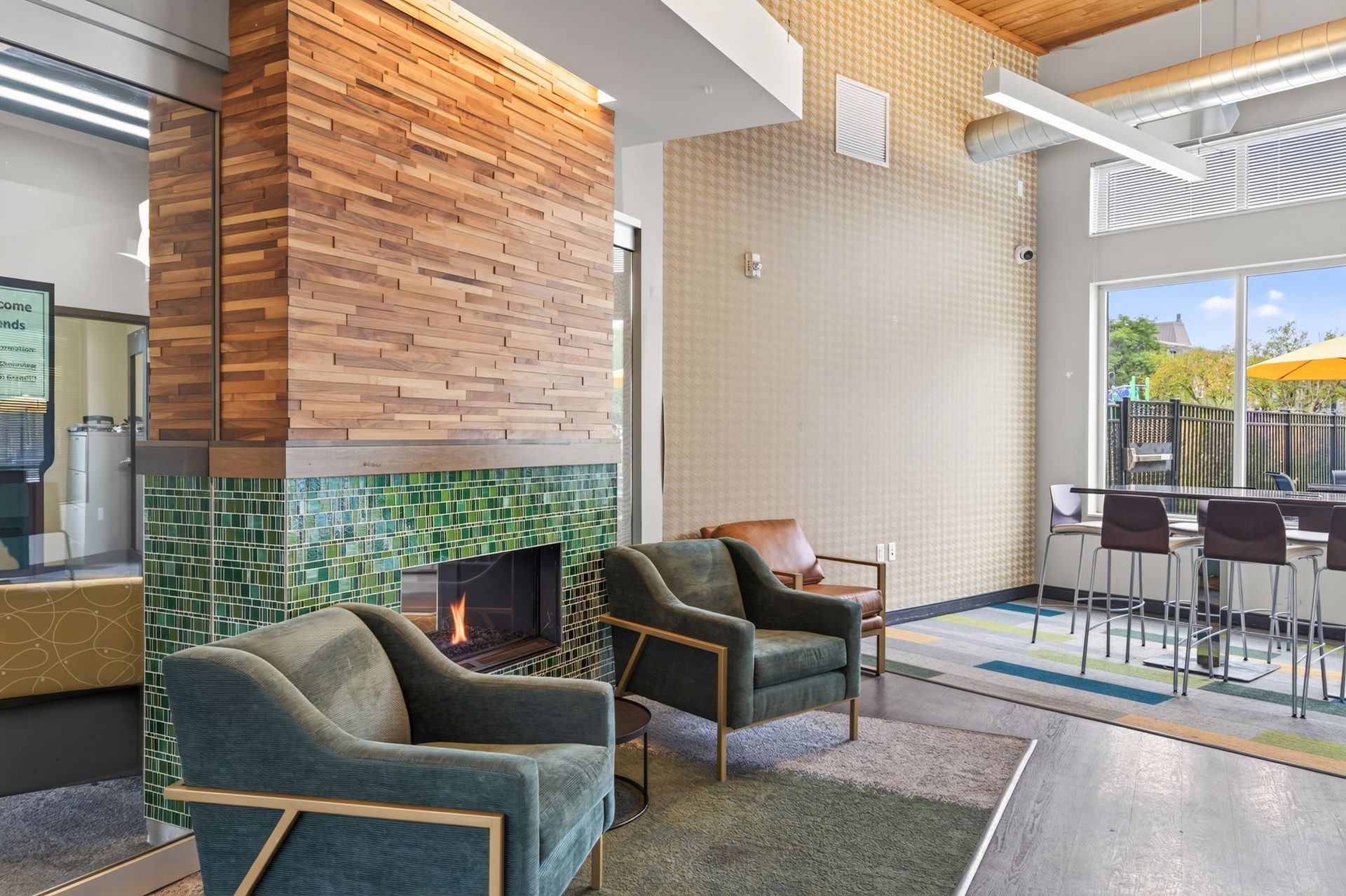 Modern lobby with green chairs, wood fireplace, and a glass-walled patio dining area