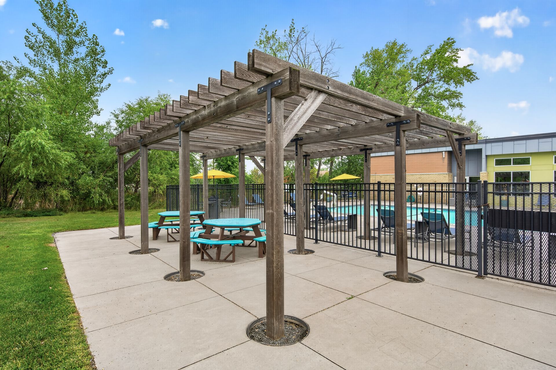 Covered picnic shelter with turquoise tables beside a pool on a sunny day