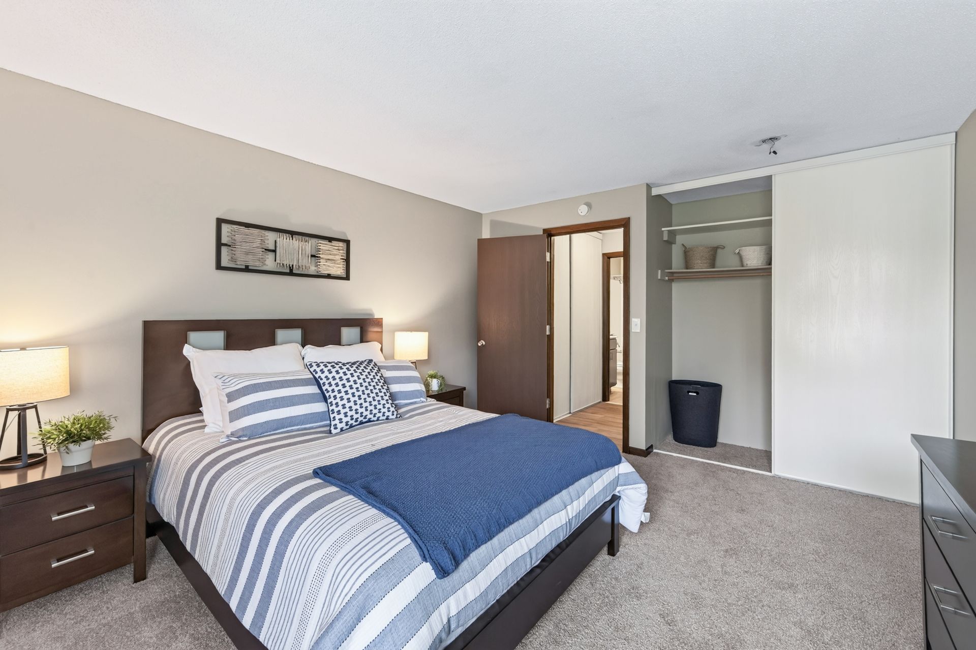 Bedroom with blue-and-white bedding, nightstands, carpet, open closet, and doorway to hallway