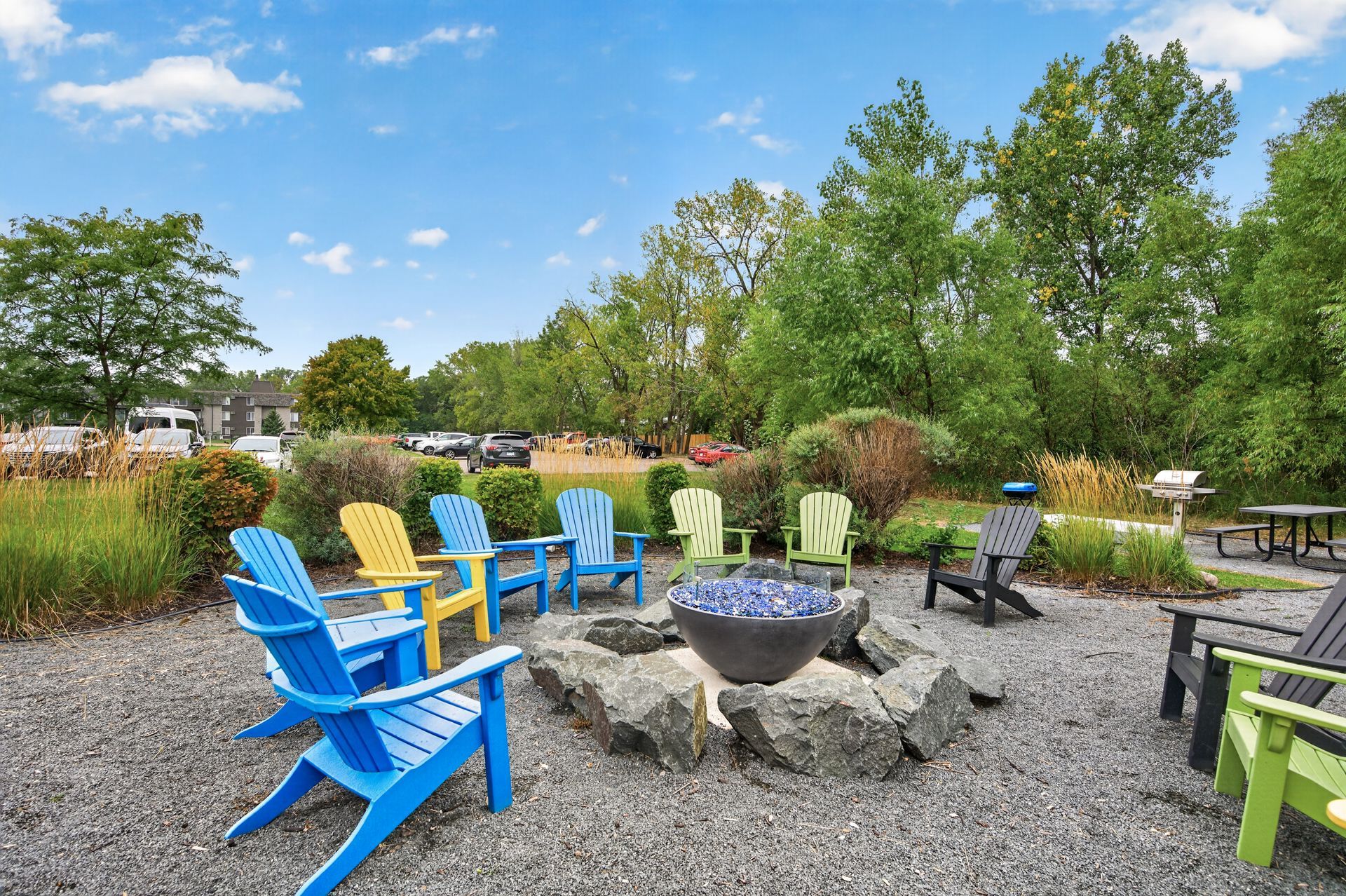 Colorful Adirondack chairs around a fire pit in a gravel garden under a blue sky.