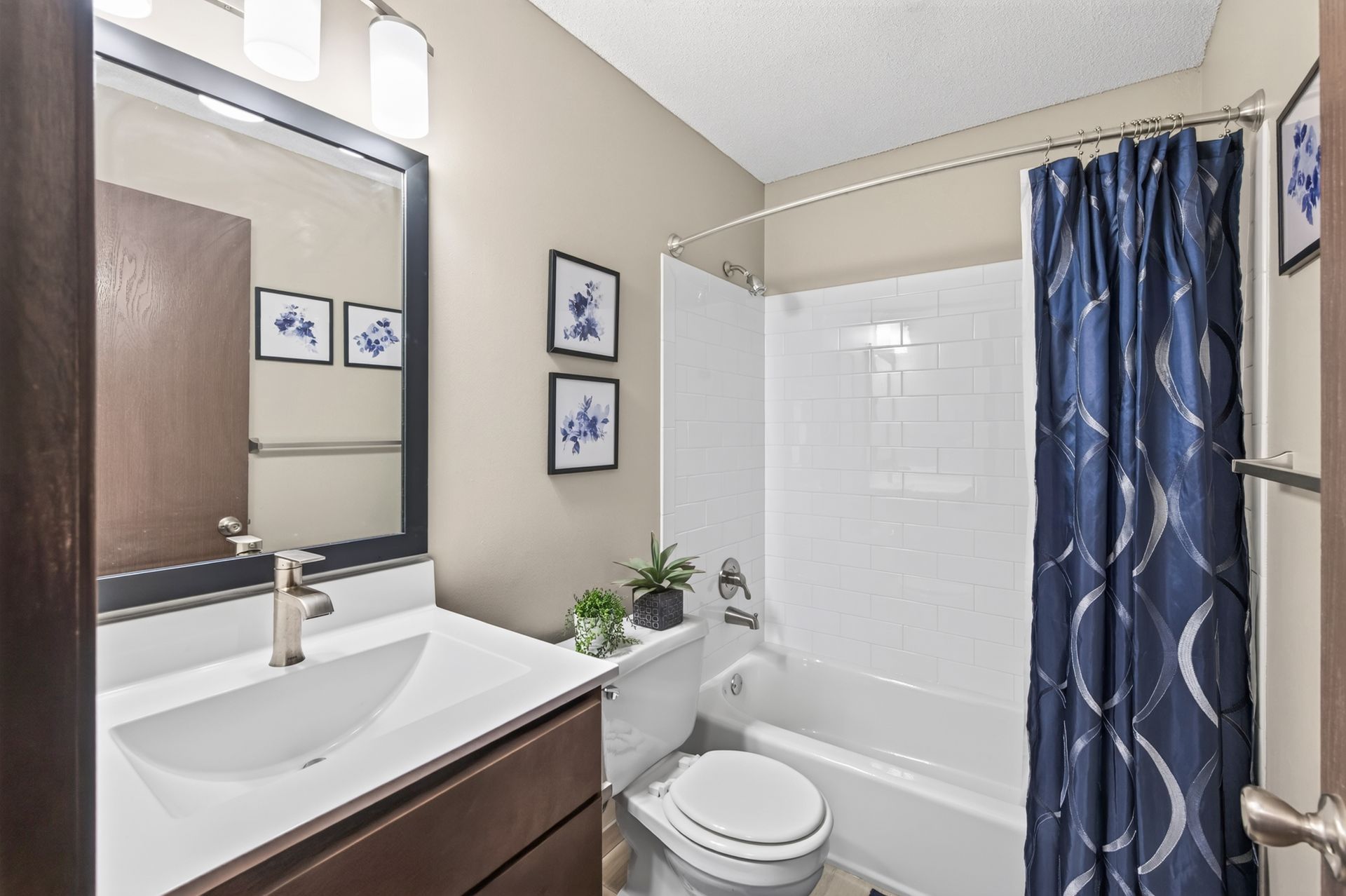 Small bathroom with vanity, toilet, mirror, and white tub with blue shower curtain.