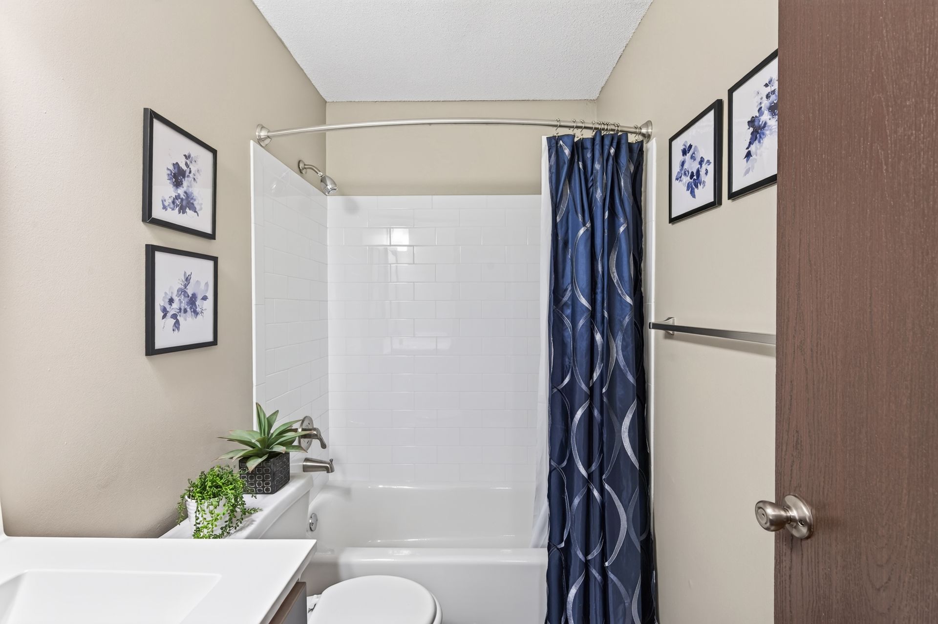 Small bathroom with shower, blue curtain, toilet, sink, and framed wall art