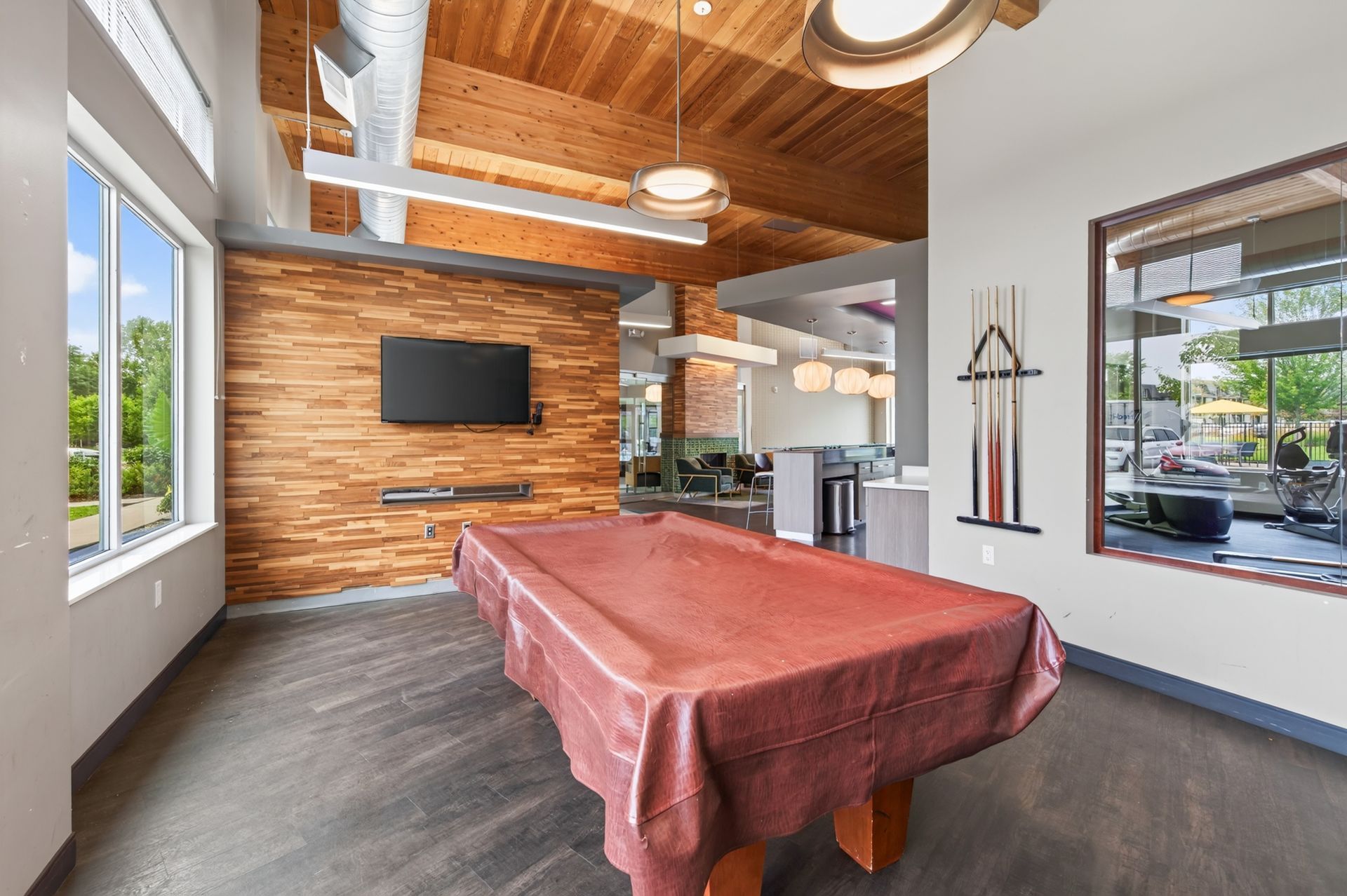 Pool table in a bright game room with wood ceiling, wall-mounted TV, and large windows