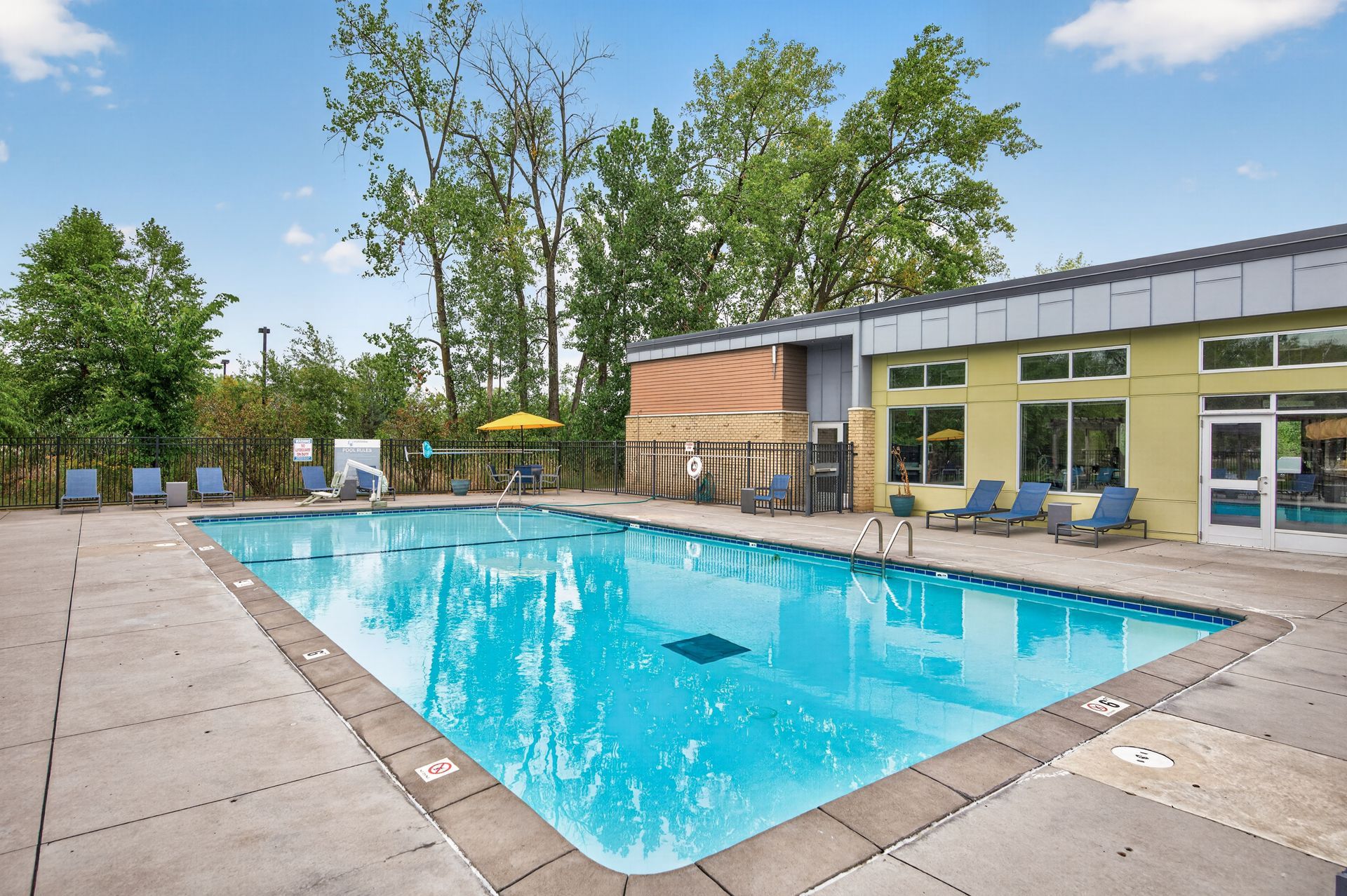 Outdoor swimming pool beside a modern building with lounge chairs and trees
