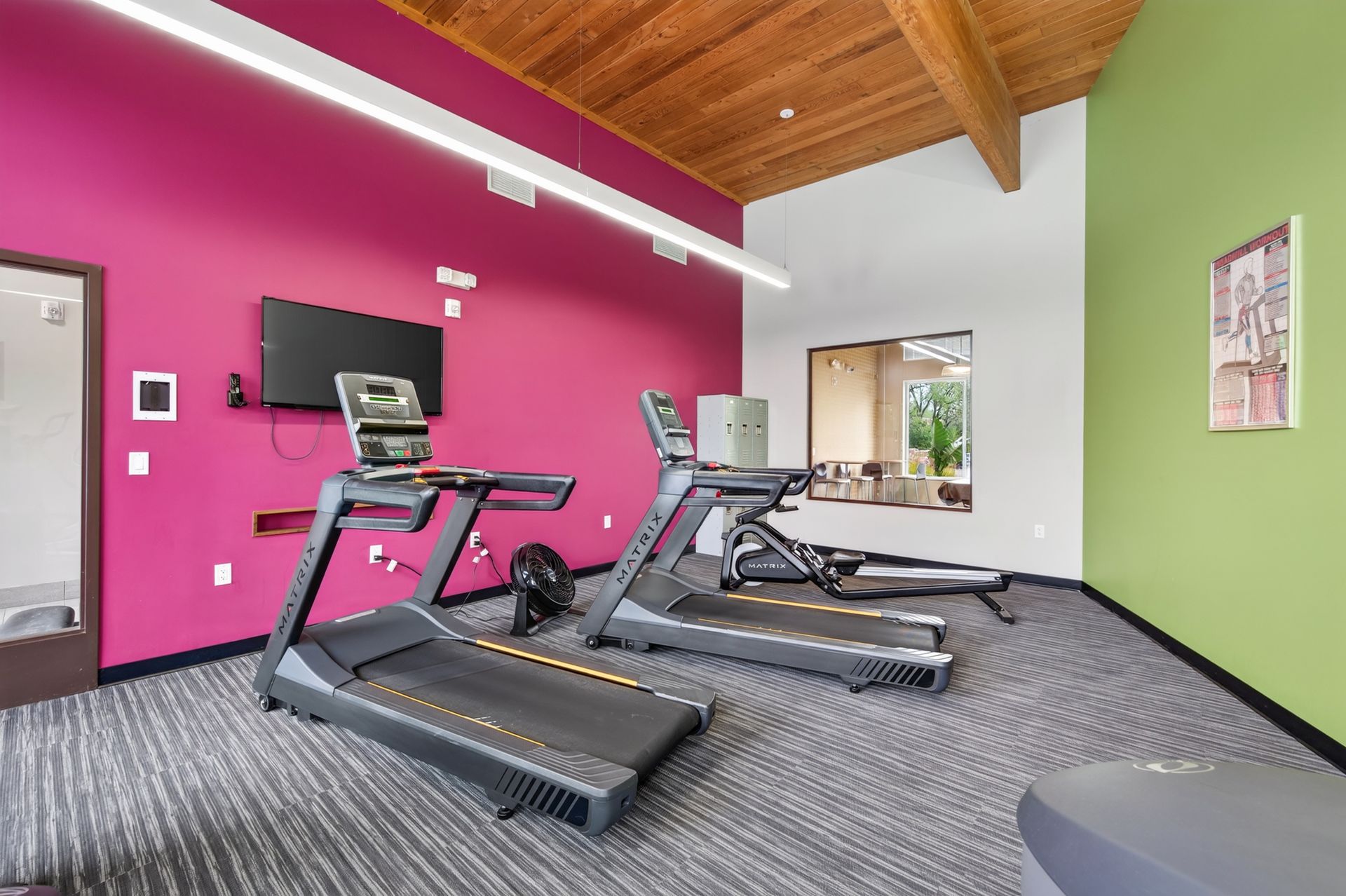 Gym with treadmills, wall-mounted TV, pink and green walls, and wood-beamed ceiling