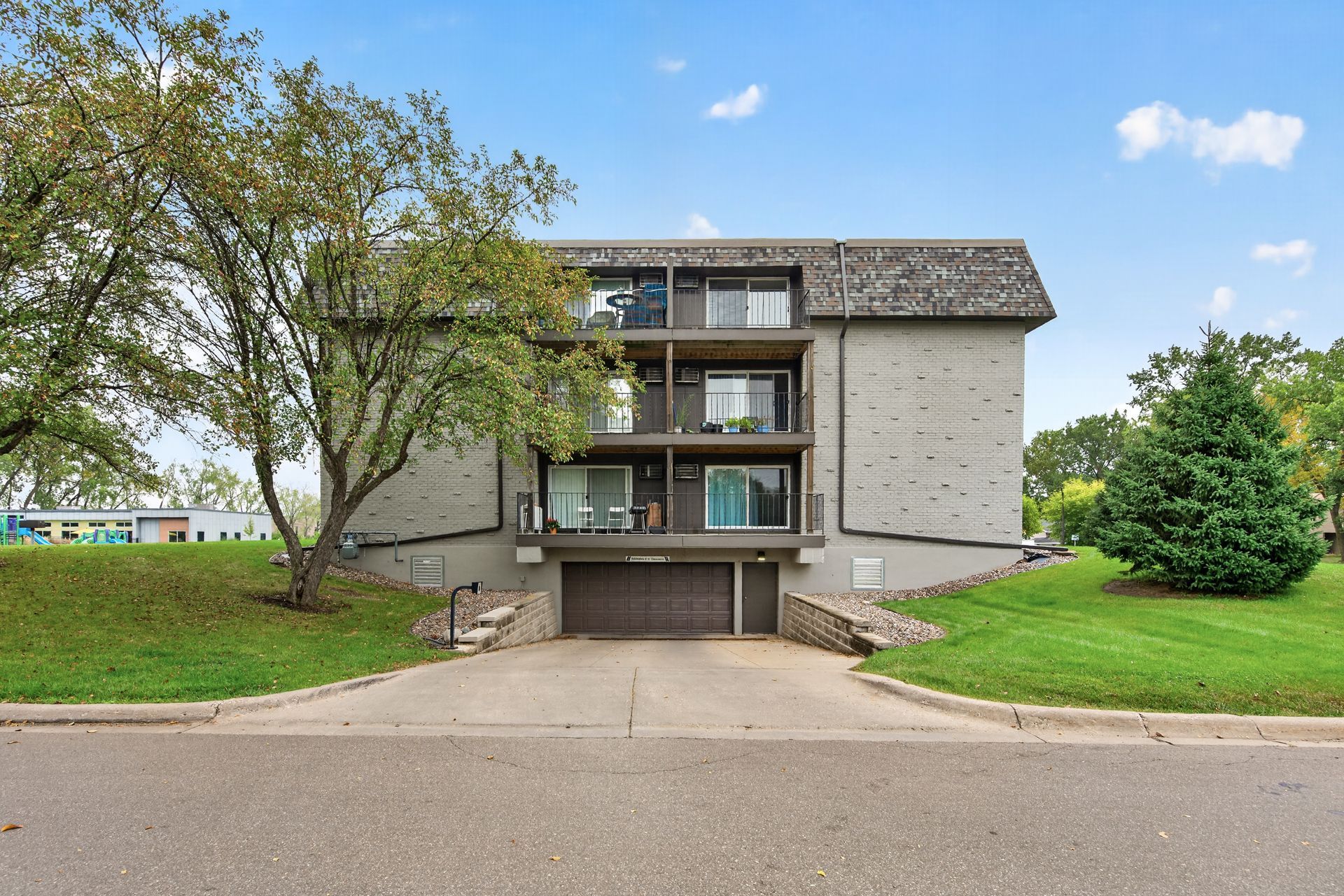 Apartment building with balconies, a tree on the left, and a paved driveway in front