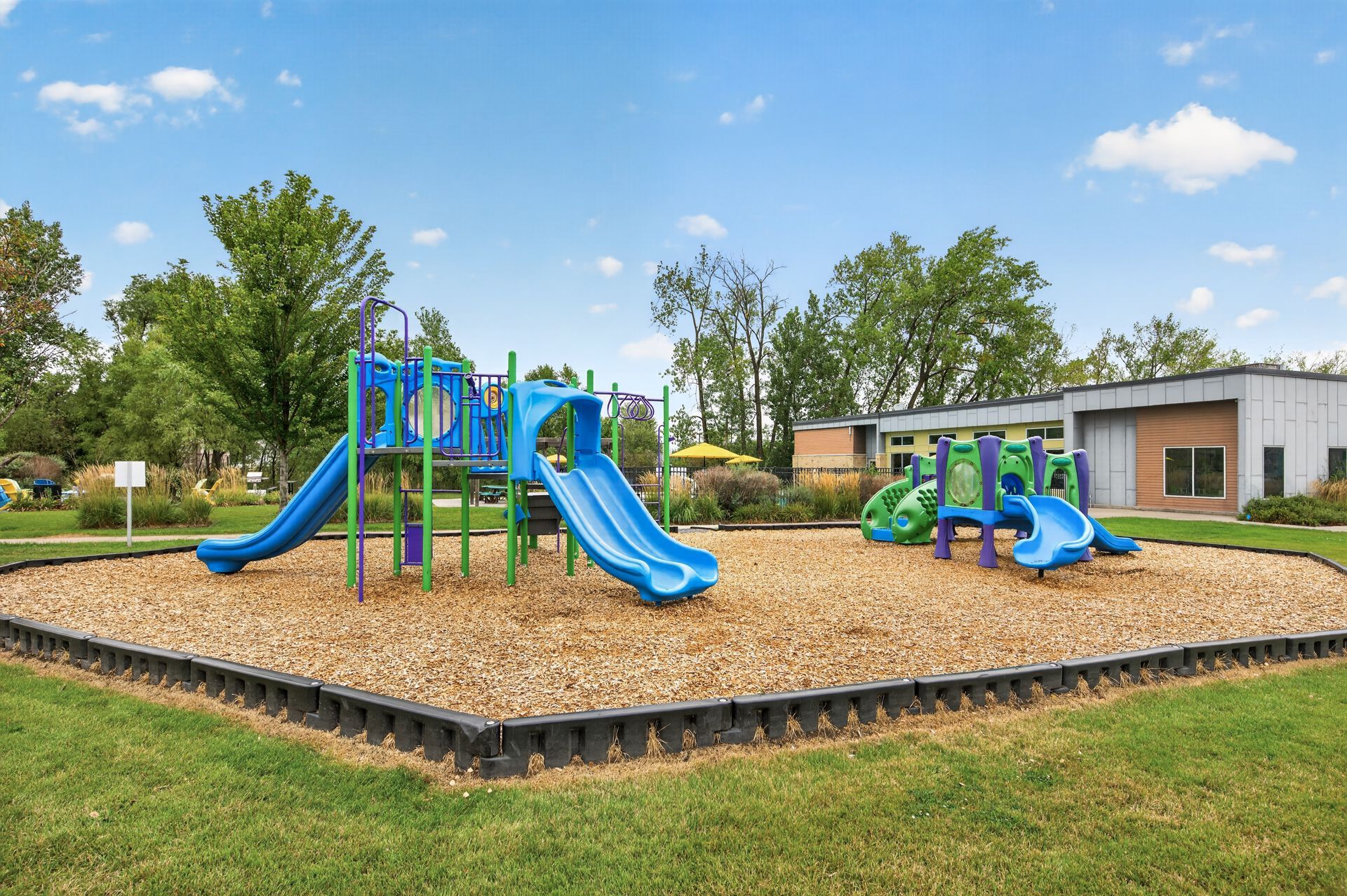 Colorful playground with slides and climbing structures on a mulch pad in a grassy park