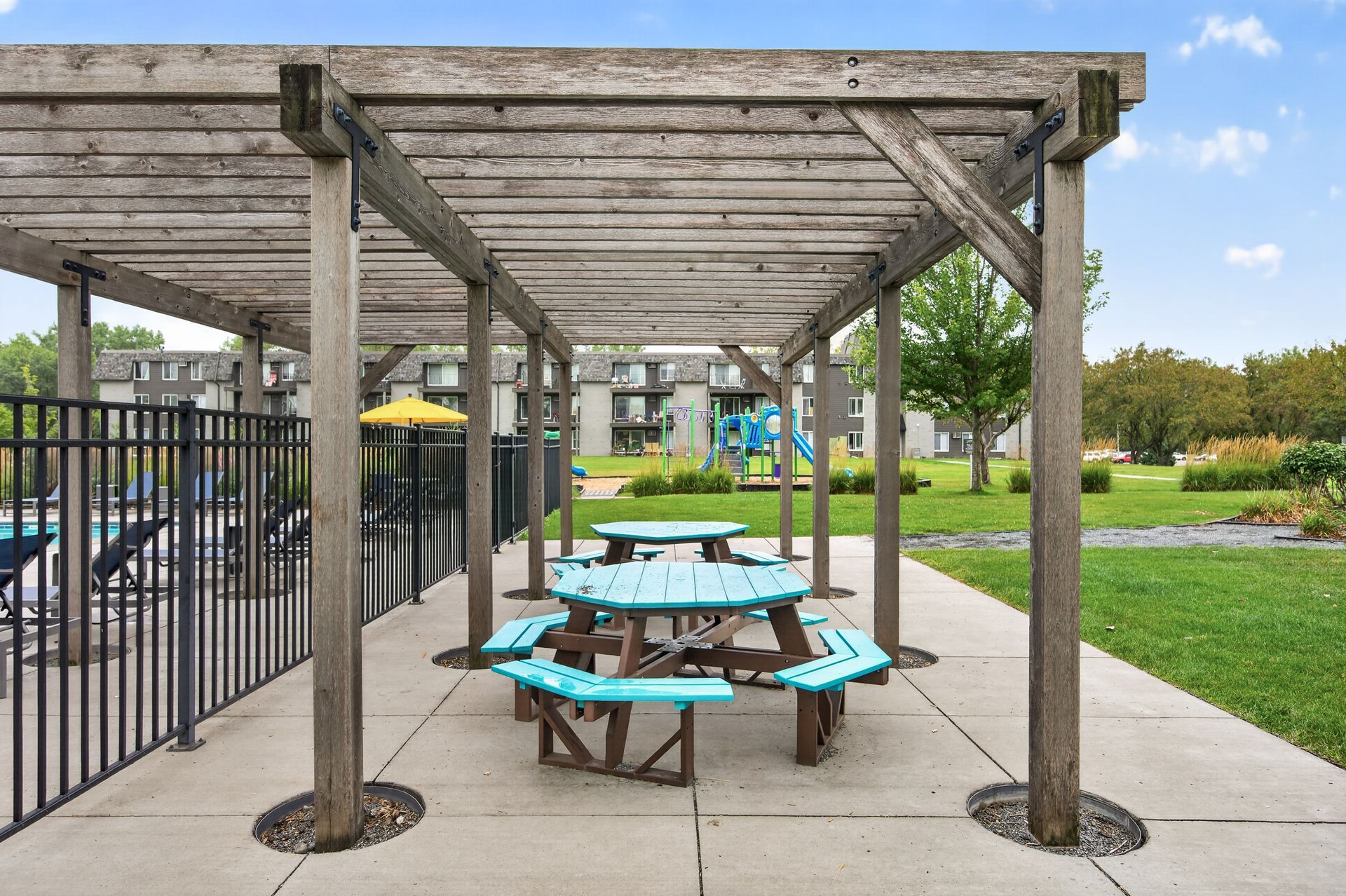 Wooden pergola over turquoise picnic tables beside a playground in a park
