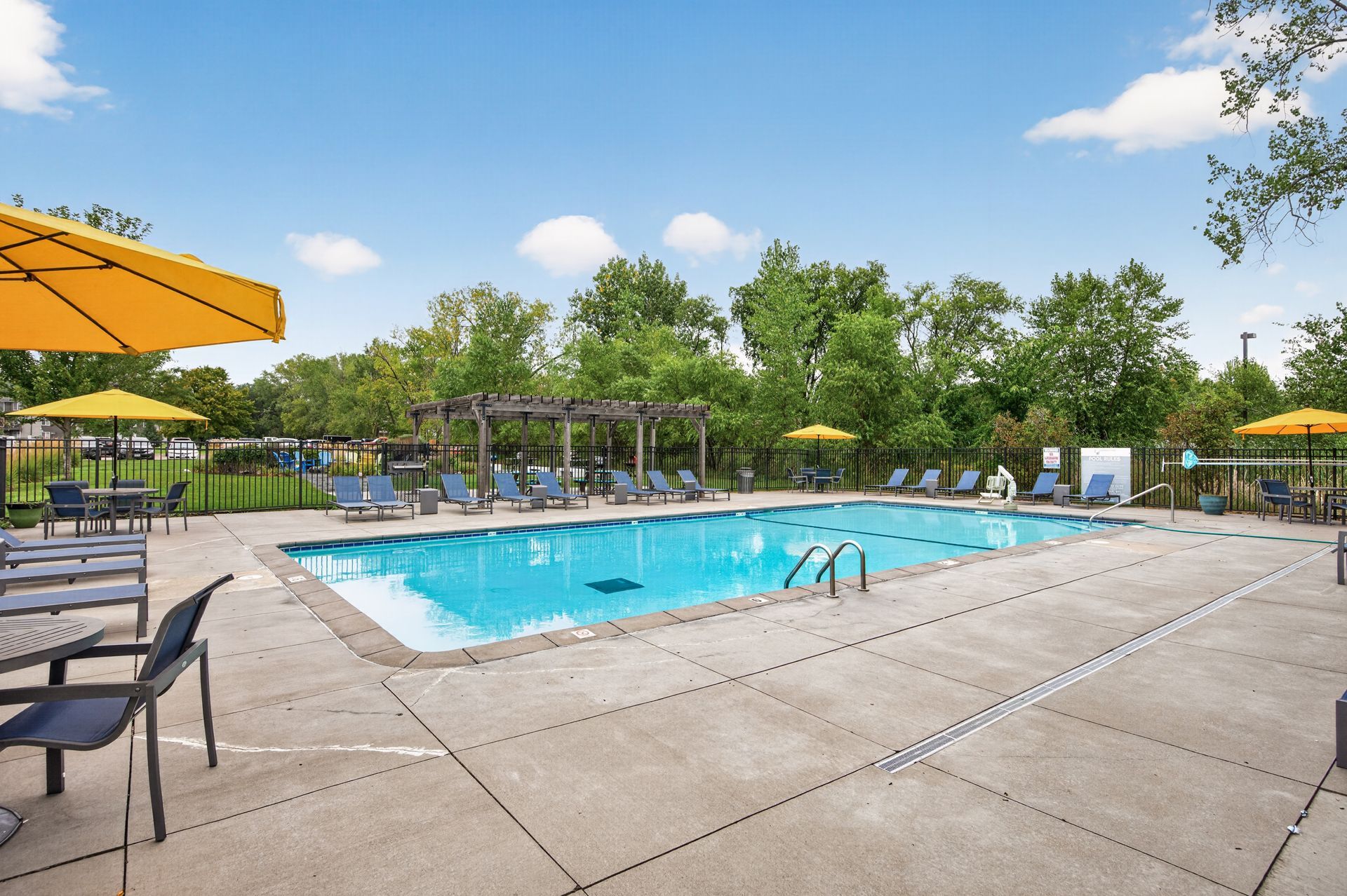Outdoor swimming pool with lounge chairs, umbrellas, and trees on a sunny day