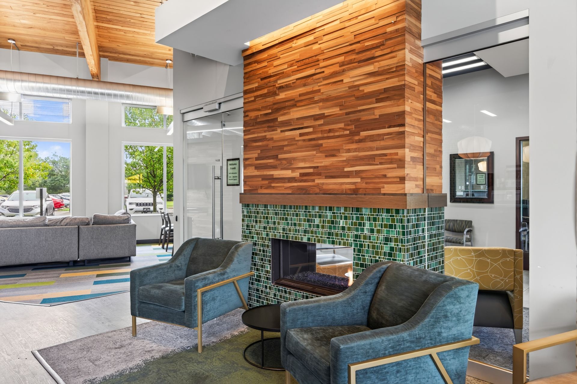 Modern lobby with teal chairs, stone fireplace, wood ceiling, and large windows overlooking greenery