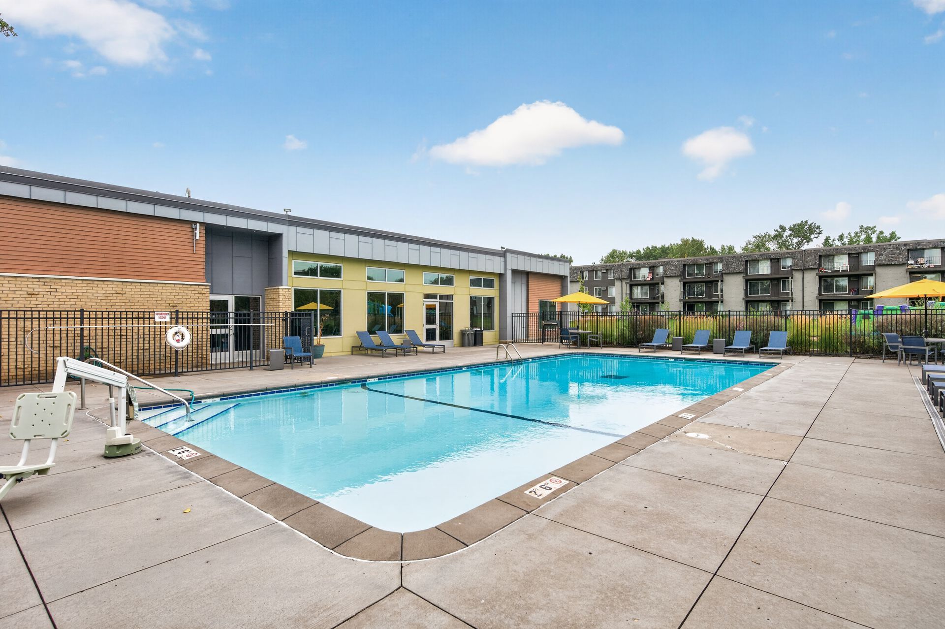 Outdoor swimming pool beside modern apartment buildings under a blue sky.