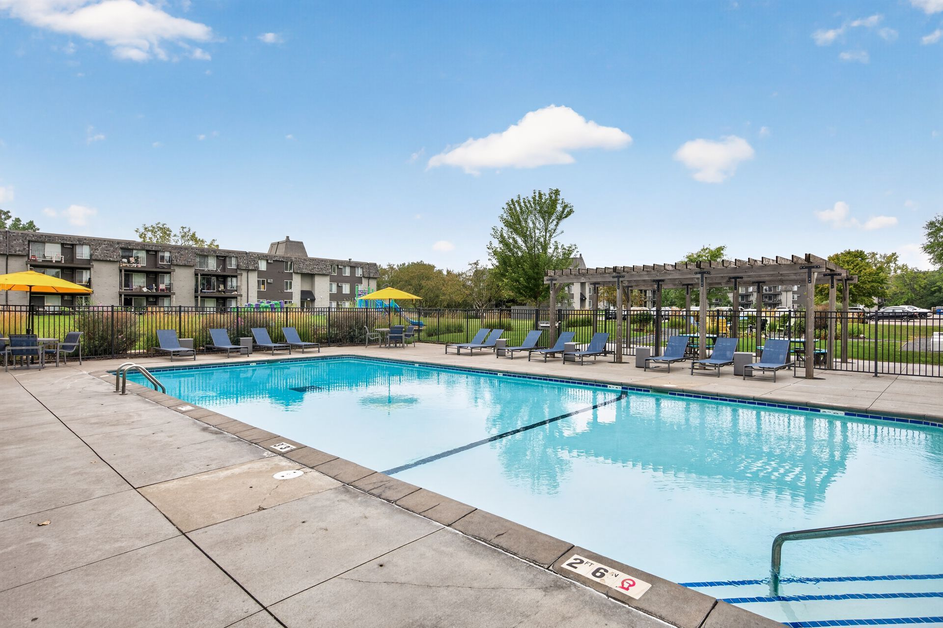 Outdoor apartment pool with lounge chairs and blue sky over a fenced deck