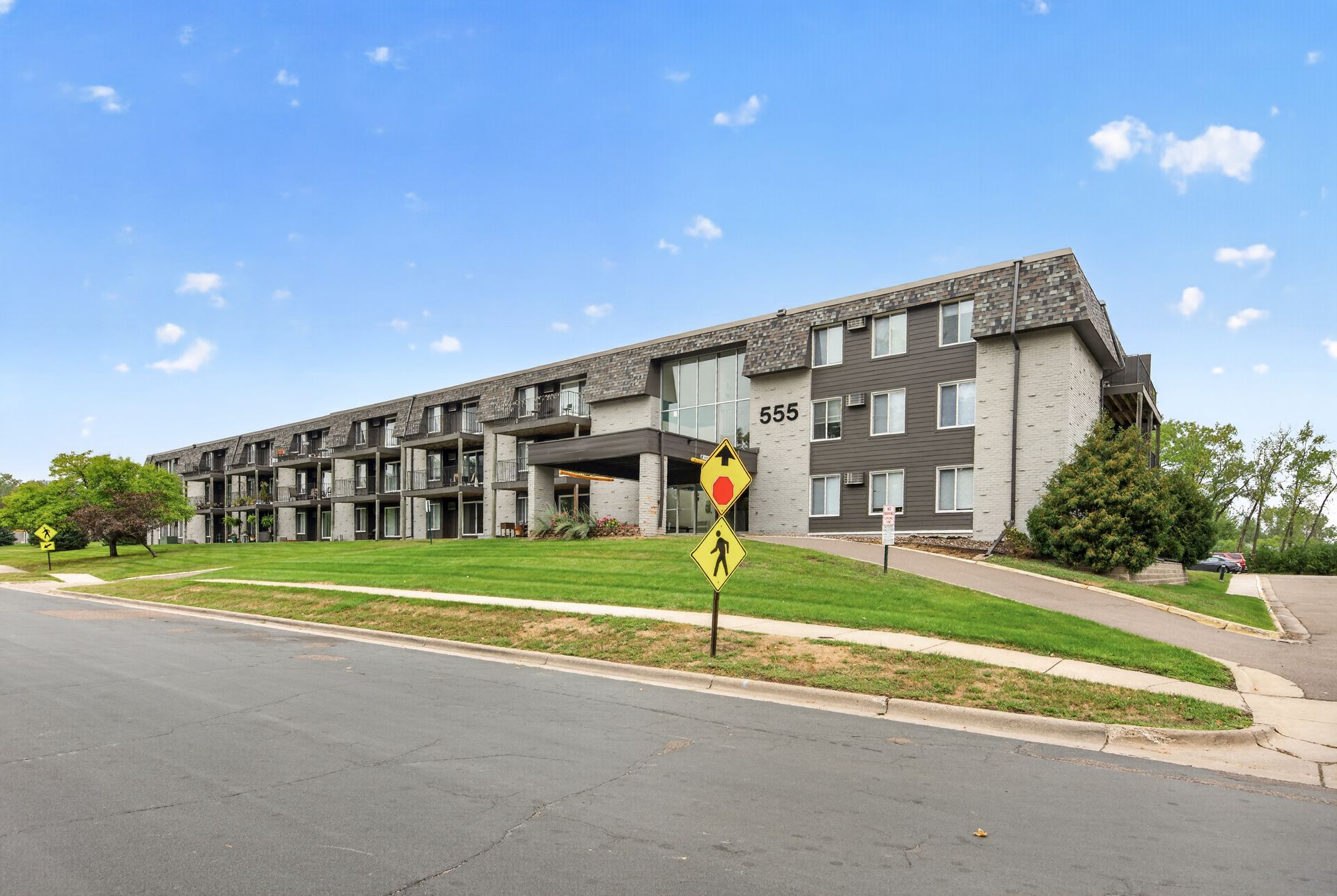 Two-story apartment building with dark siding beside a road under a blue sky
