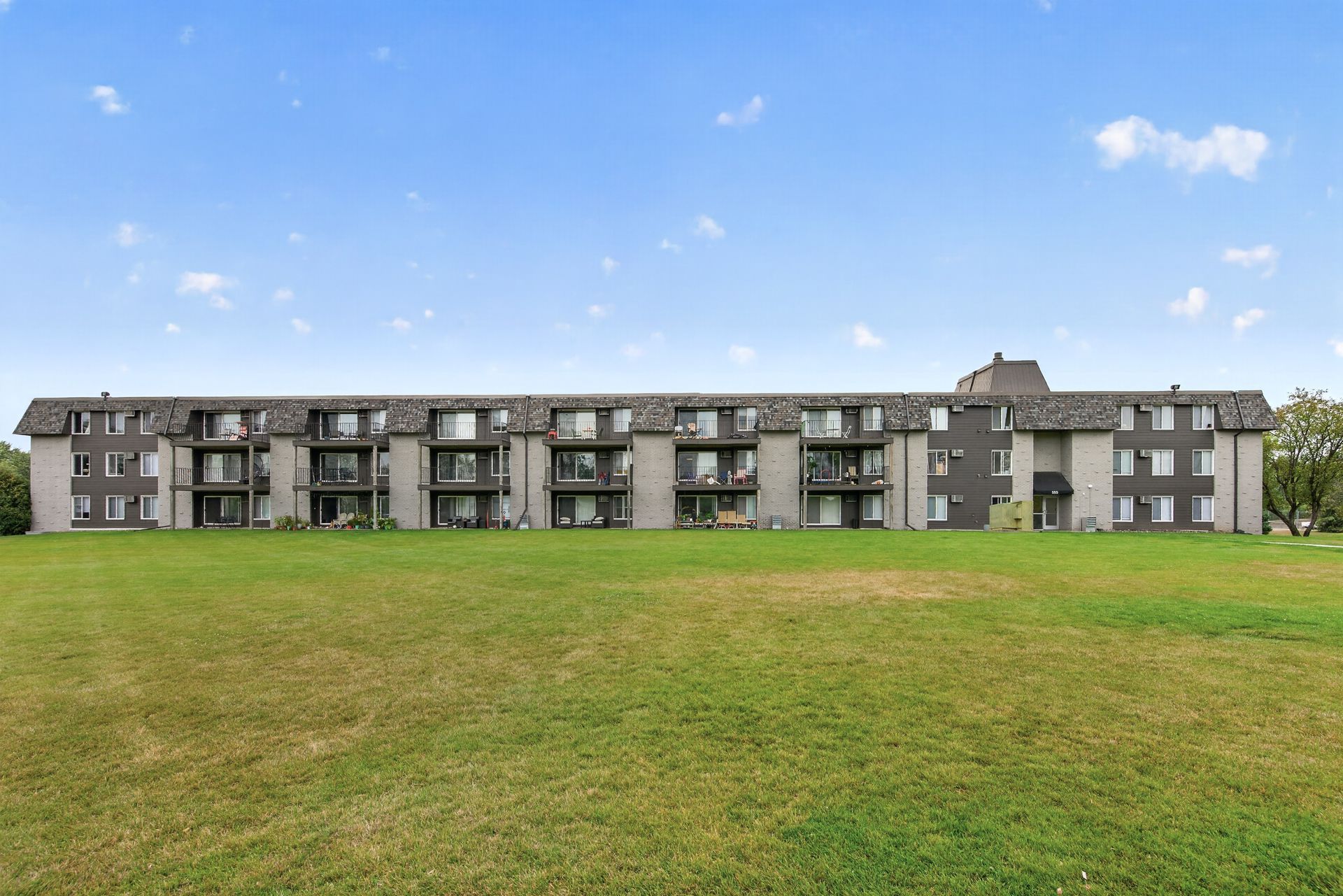 Long gray apartment building behind a wide green lawn under a blue sky