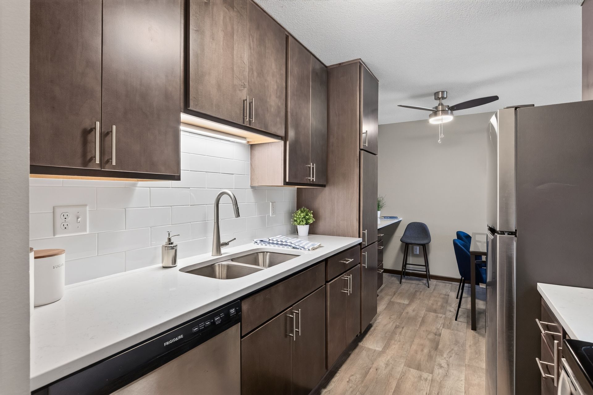 Modern kitchen with dark wood cabinets, white countertops, stainless sink, and a dining area in the background