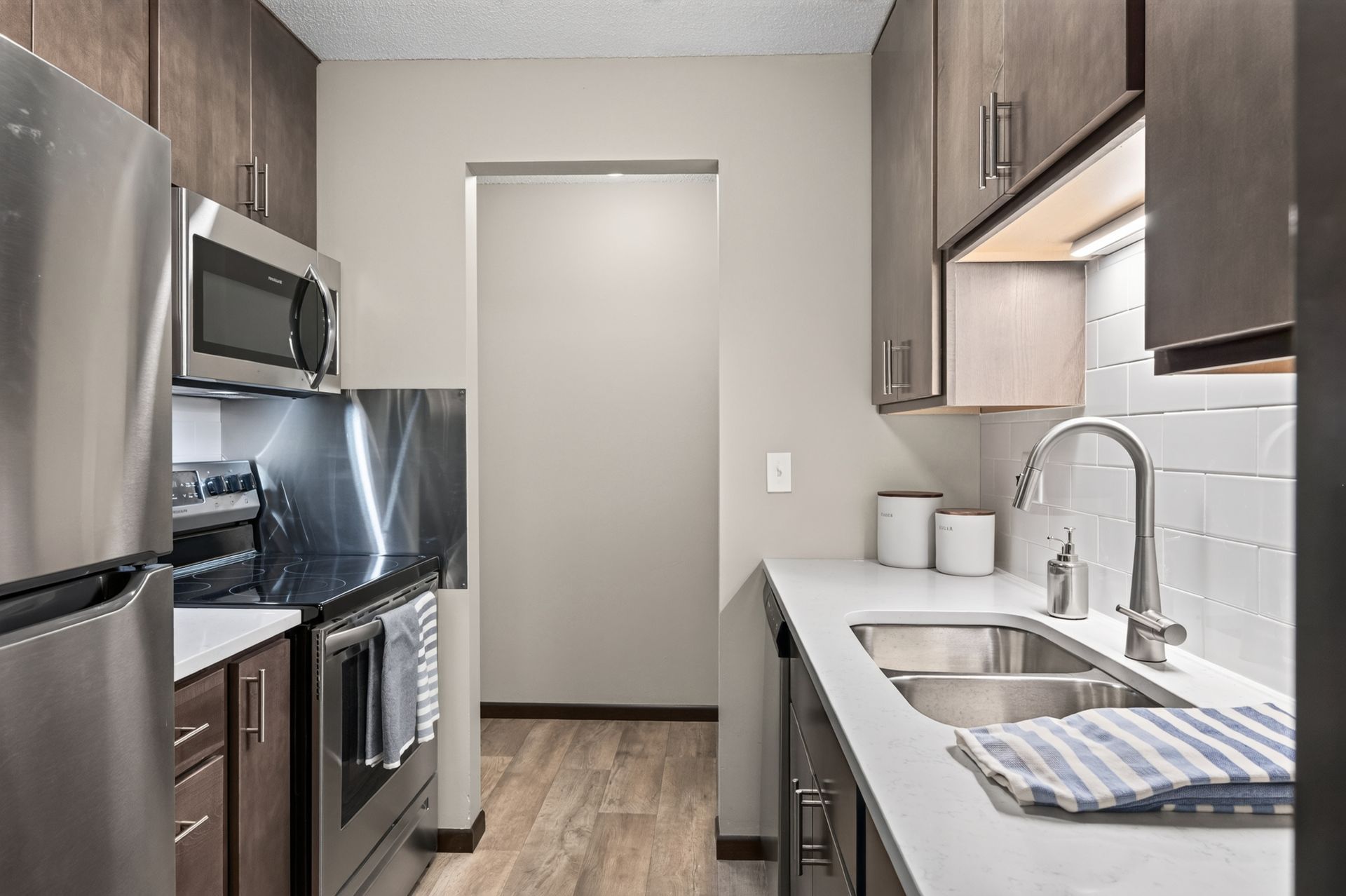 Narrow modern galley kitchen with stainless appliances, white countertops, and gray cabinets