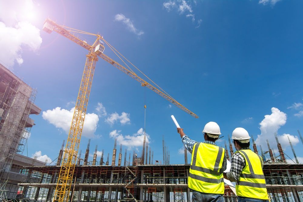 Two Construction Workers Are Looking At A Crane At A Construction Site — Calibre Engineering In Darwin, NT