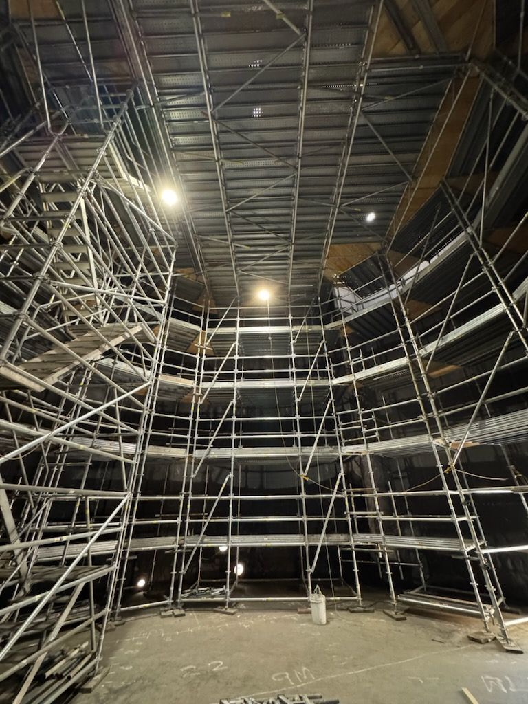 A multi-level metal scaffolding structure fills an indoor space, extending from a concrete floor to a high ceiling.