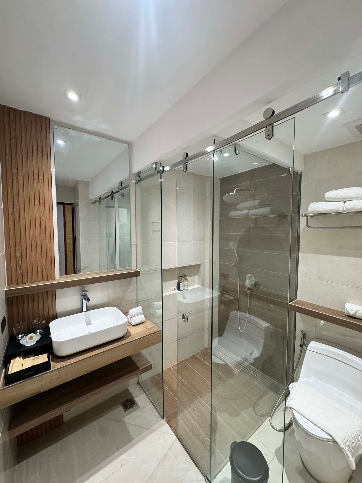 Modern bathroom with glass shower, toilet, vanity, mirrors, and folded towels