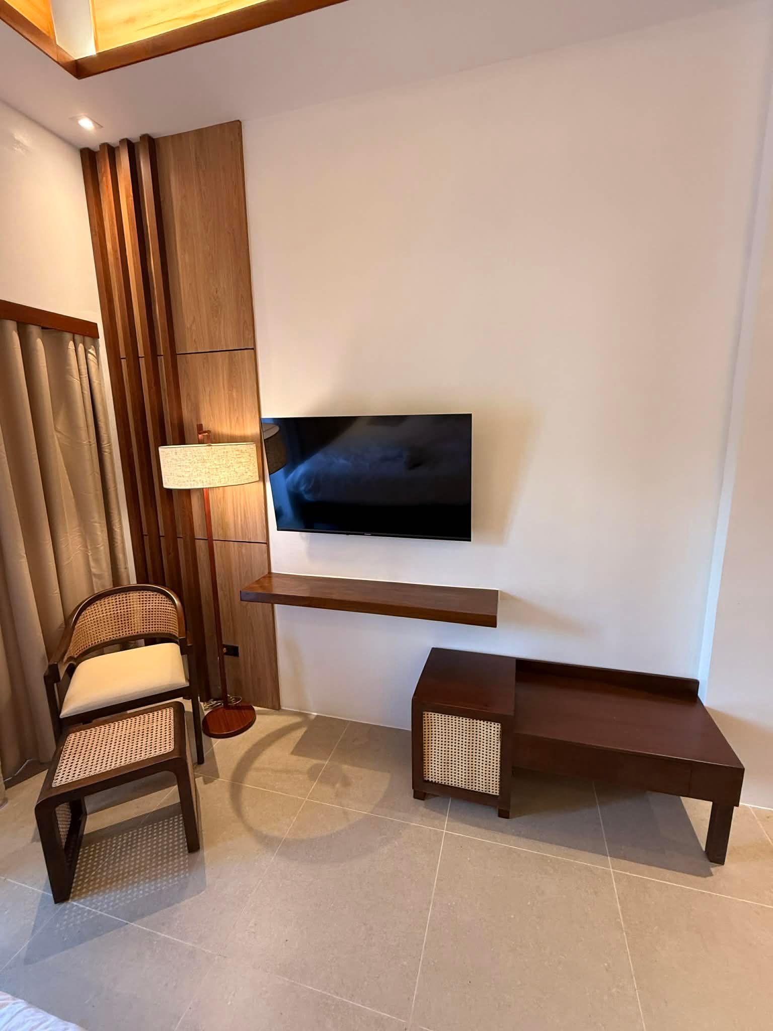 Modern living room with wall-mounted TV, wooden chair, lamp, and low coffee table against white walls.