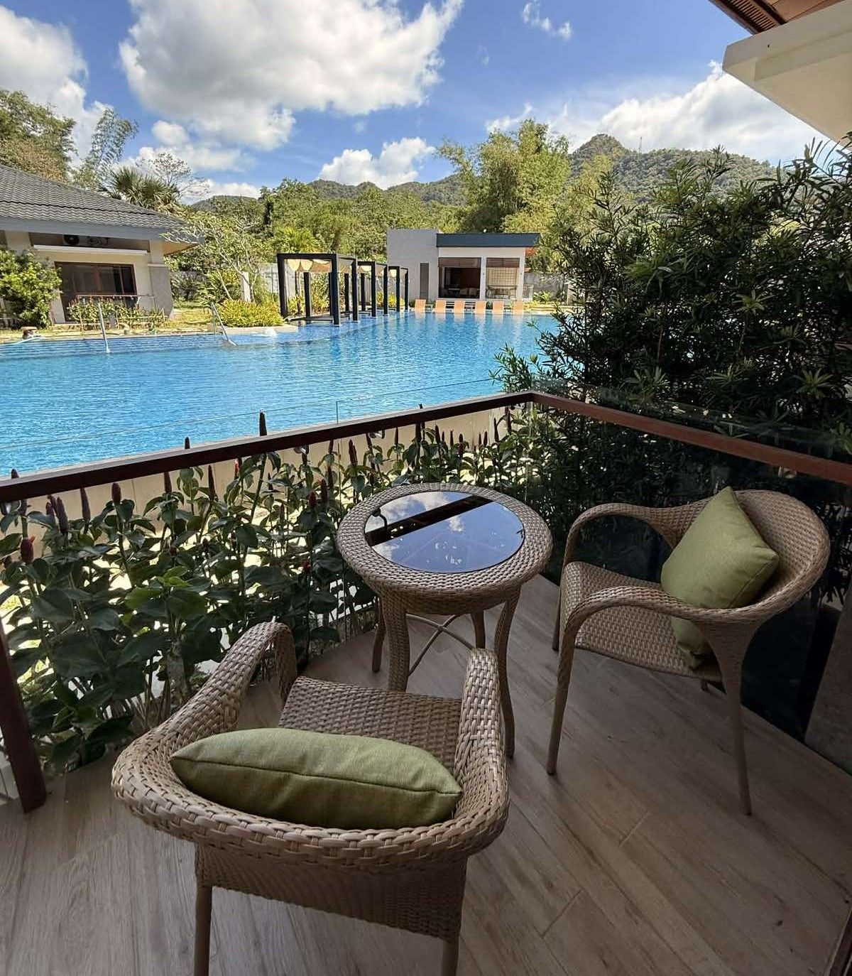 Poolside patio with wicker chairs and a small table overlooking a blue resort pool and trees