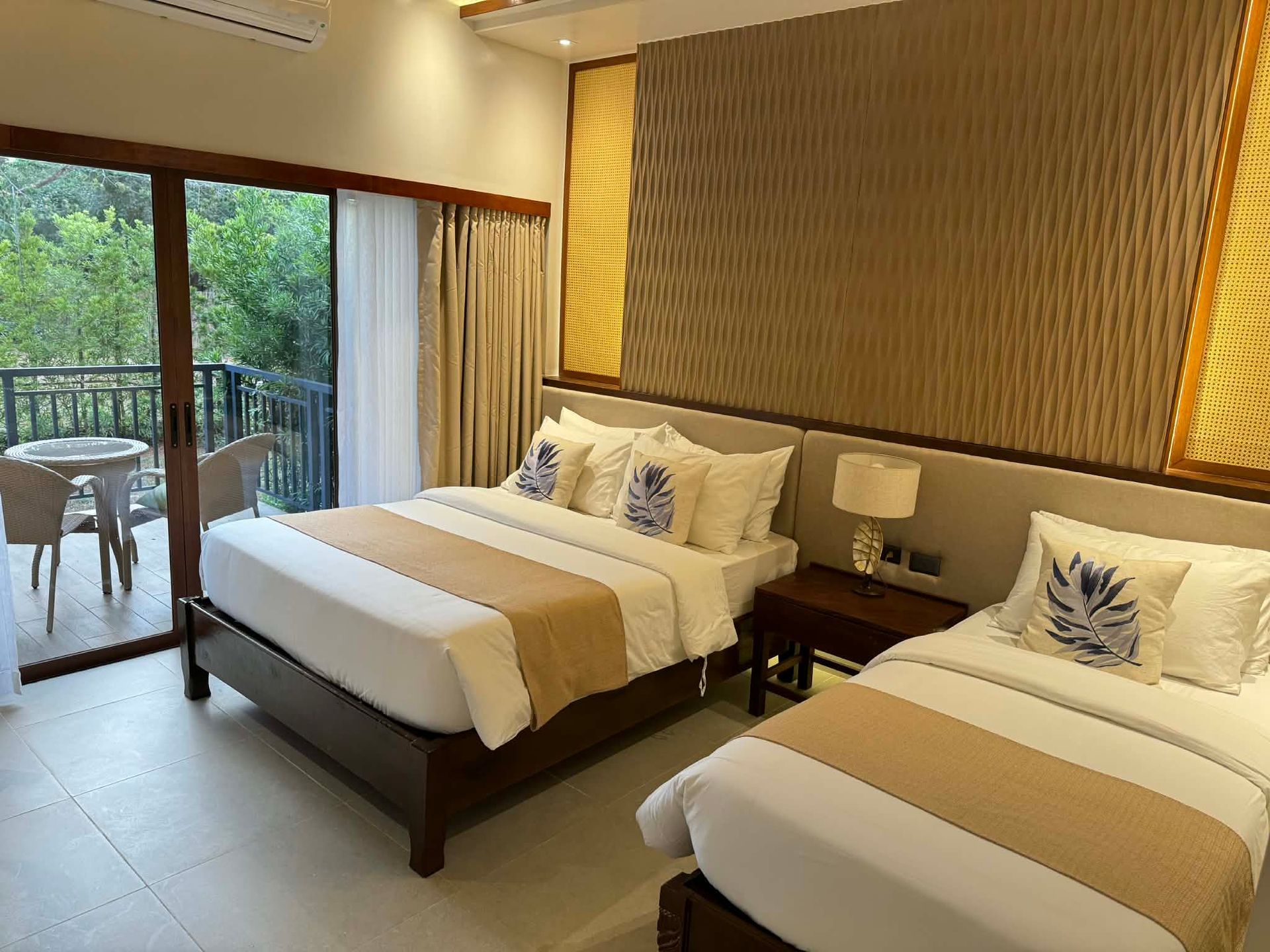 Two twin beds in a hotel room with a balcony and tropical view