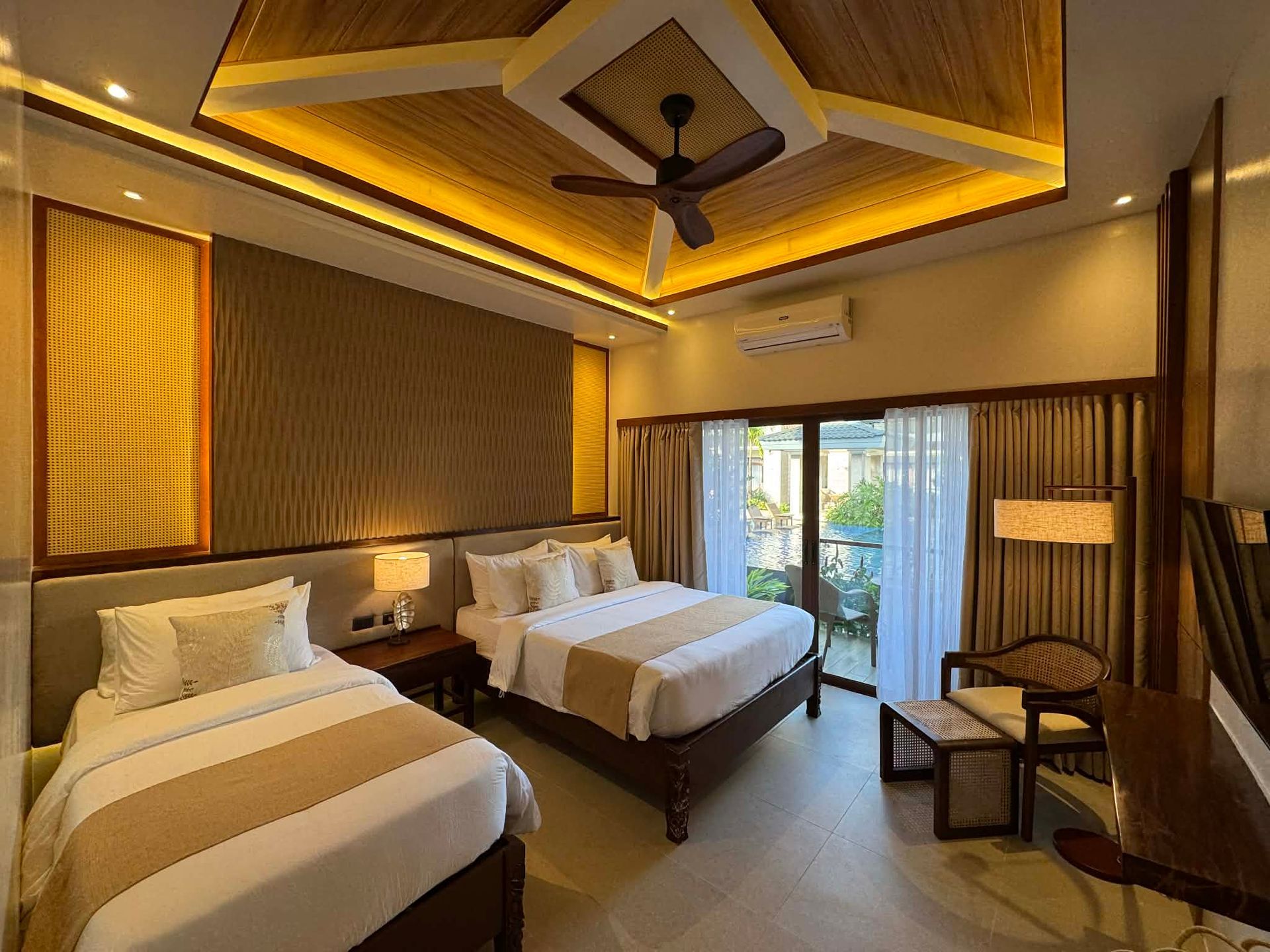 Warm hotel room with two beds, wood ceiling, and sliding doors to a balcony